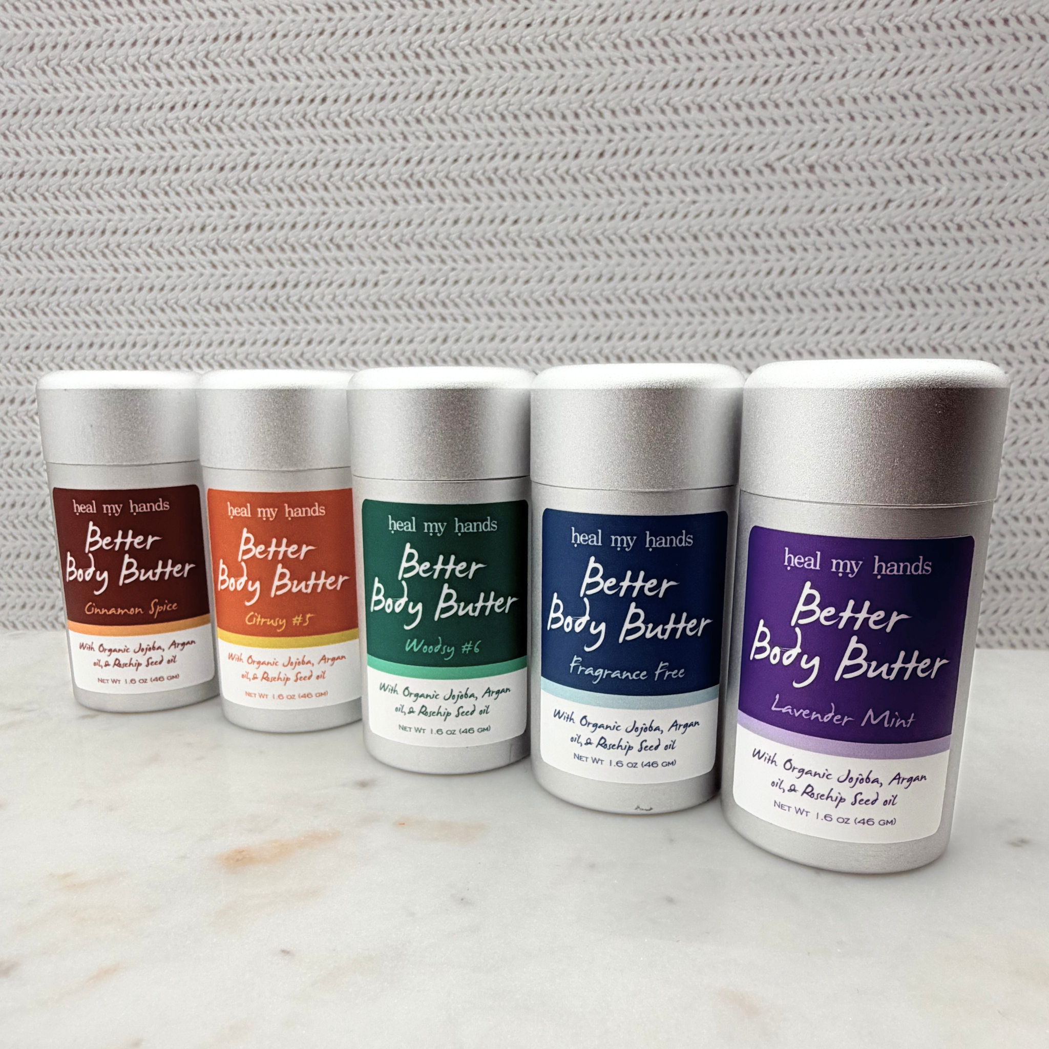 Five containers of 'Better Body Butter' with different colored labels on a marble surface.