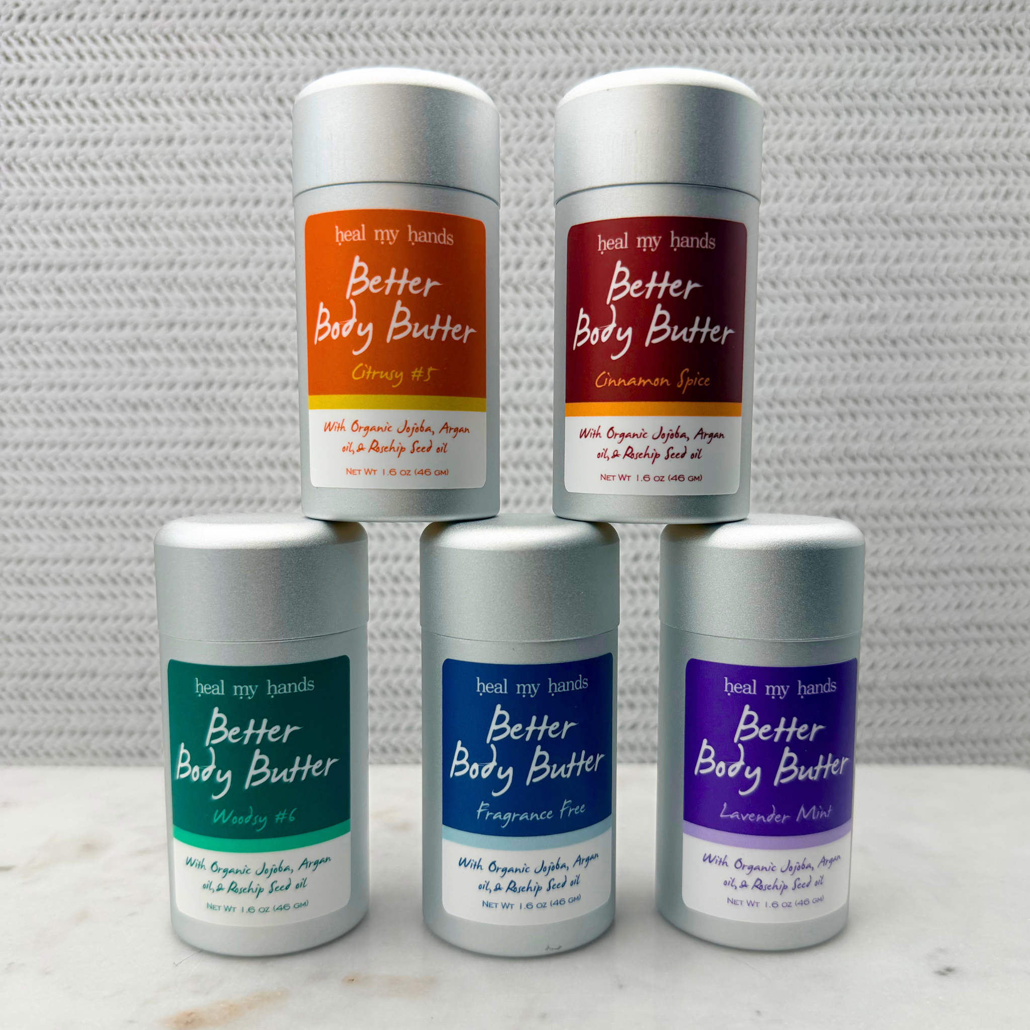 Five containers of Better Body Butter in different scents on a textured white background