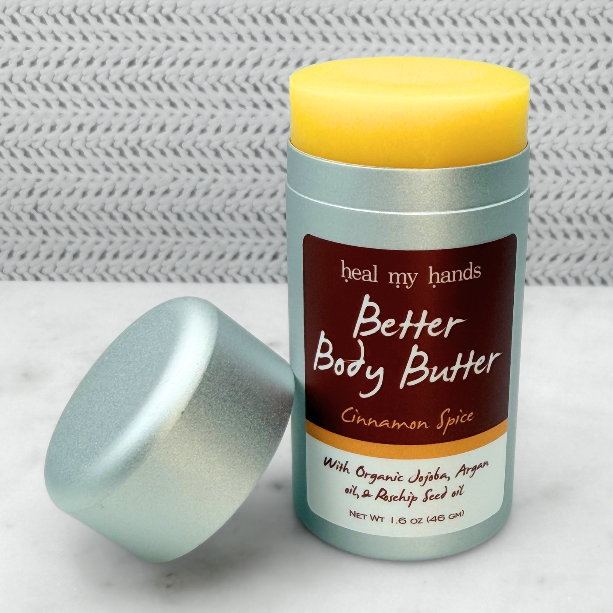 Open push up tube of Better Body Butter in Cinnamon Spice on a textured surface.