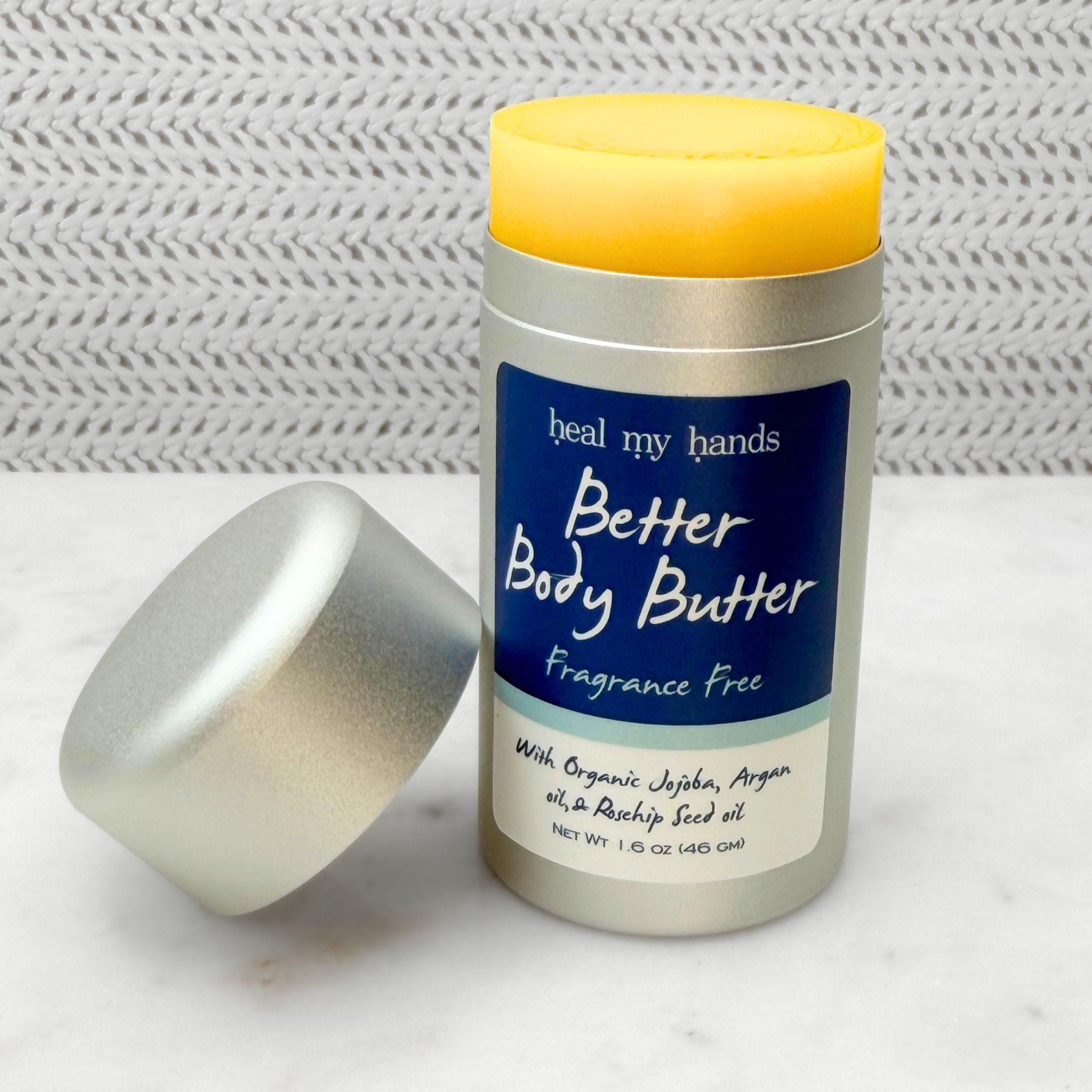 Open push up tube of Better Body Butter in Fragrance Free on a textured surface.