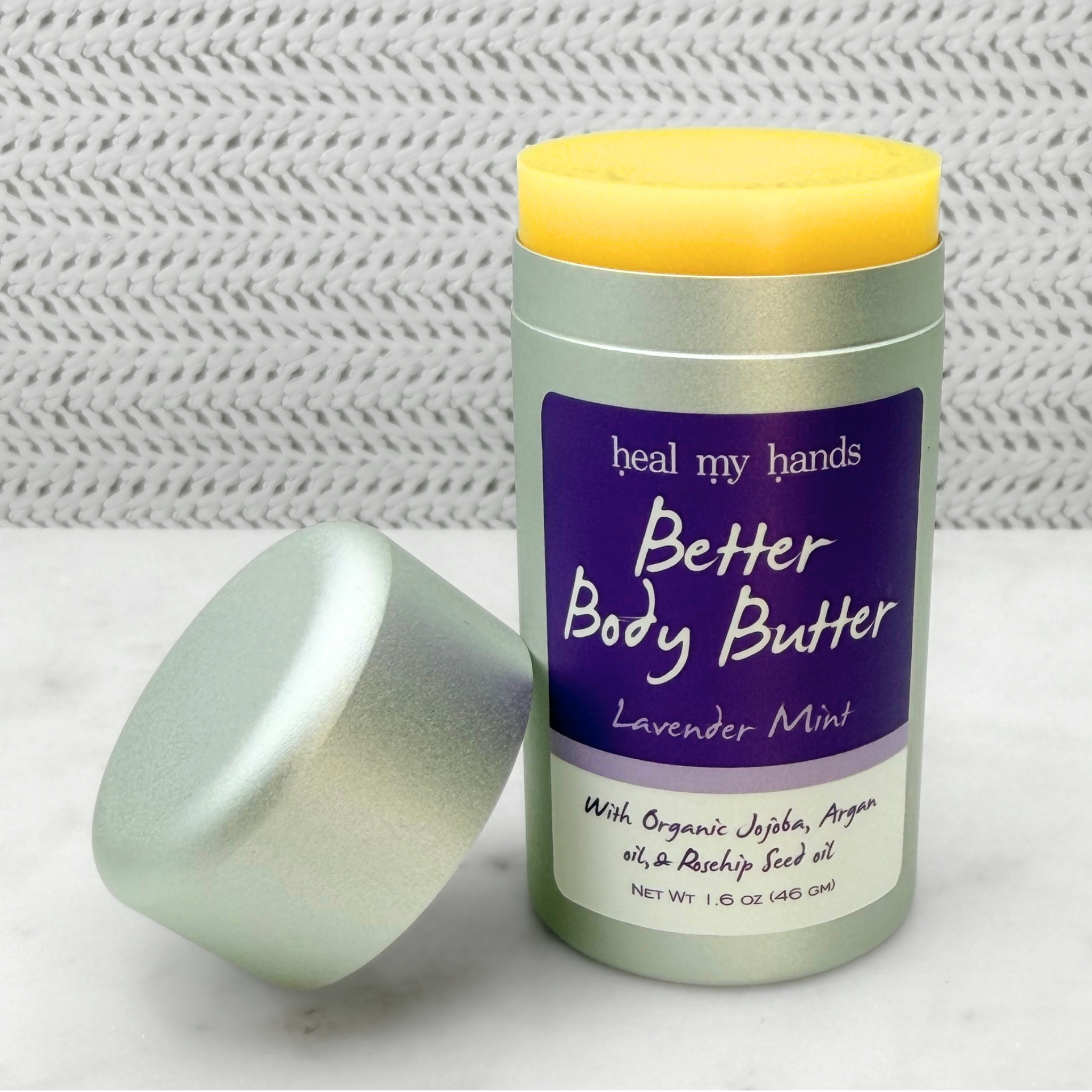 Open push up tube of Better Body Butter in Lavender Mint on a textured surface.