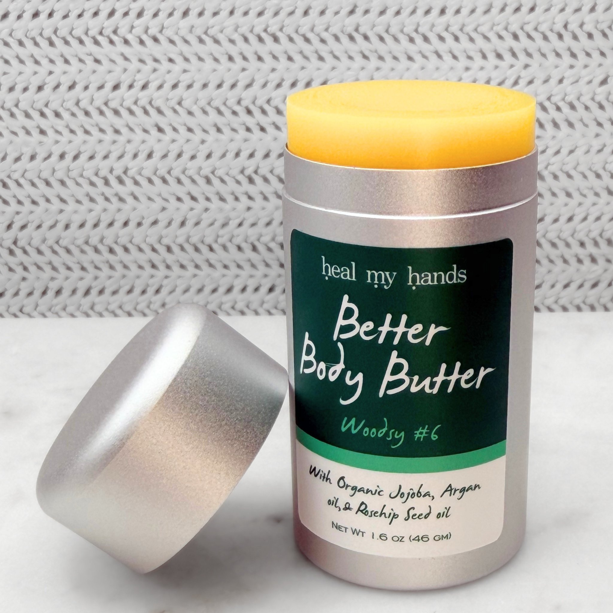 Open push up tube of Better Body Butter in Woodsy #6 on a textured surface.