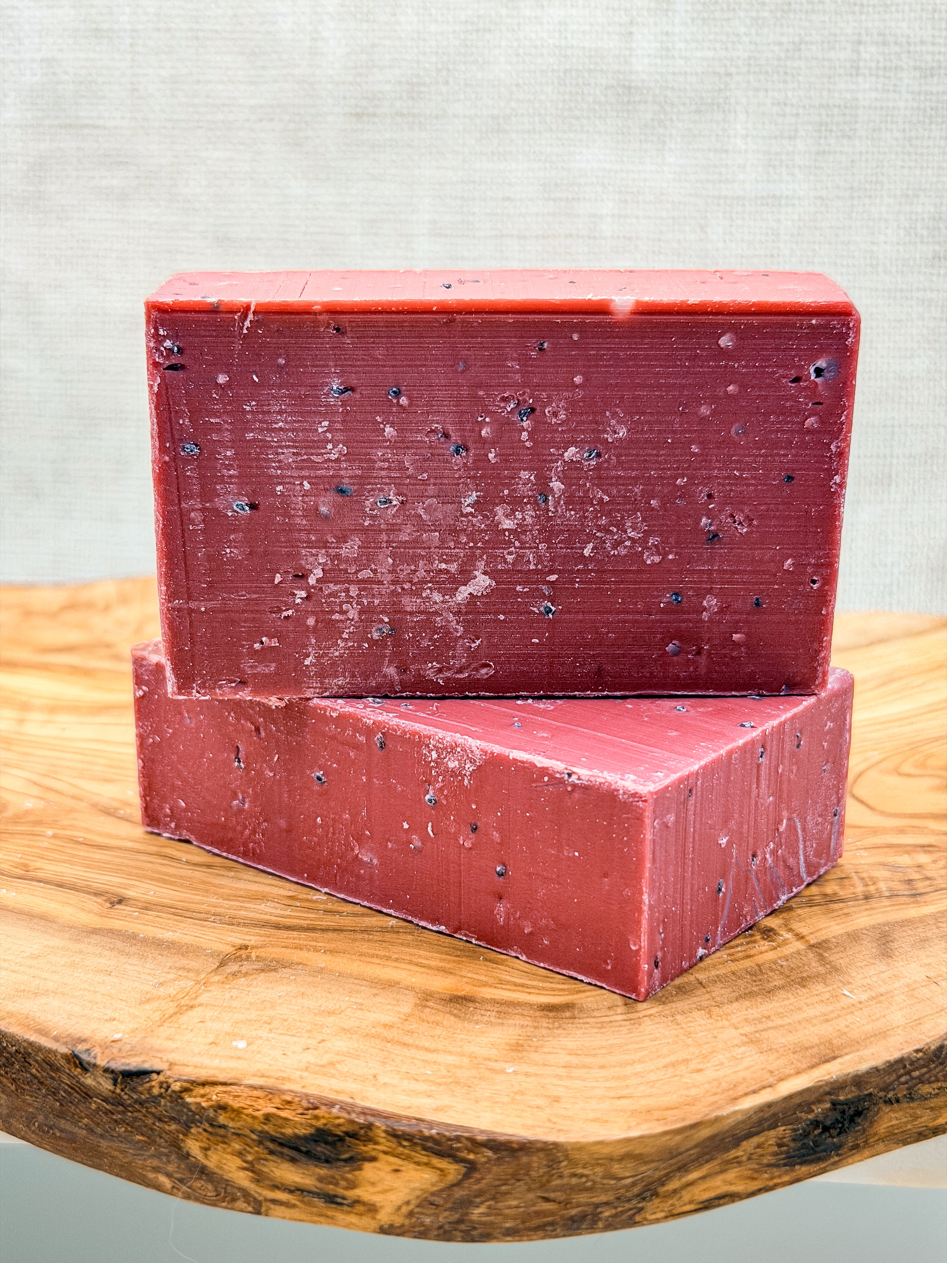 Two red soap bars stacked on a wooden surface with a gray background