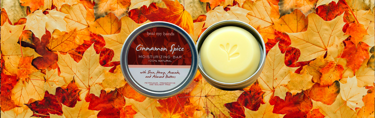 An open tin of Heal My Hands Cinnamon Spice Moisturizing Bar on top of scattered autumn leaves.