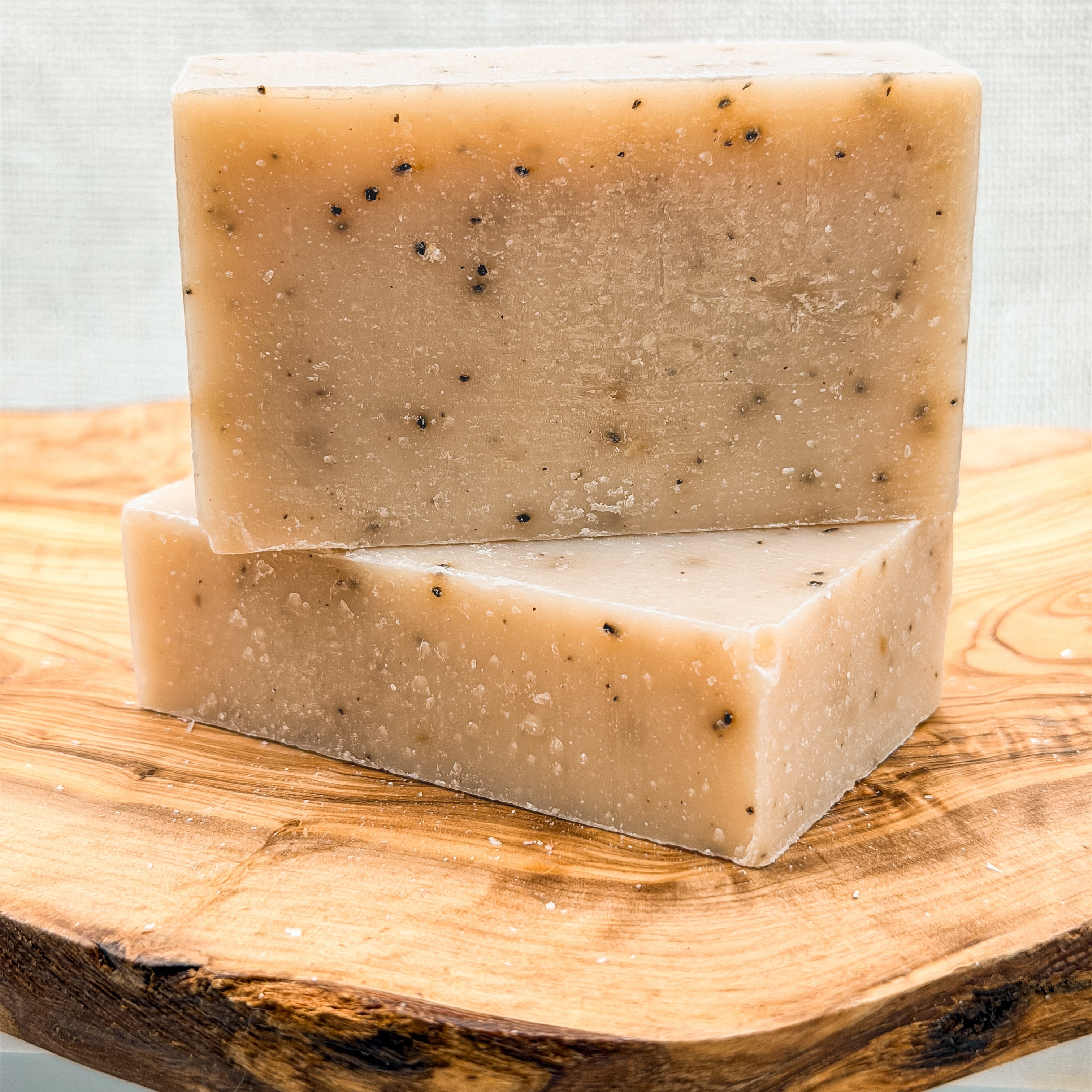 Two bars of soap stacked on a wooden surface with a light background