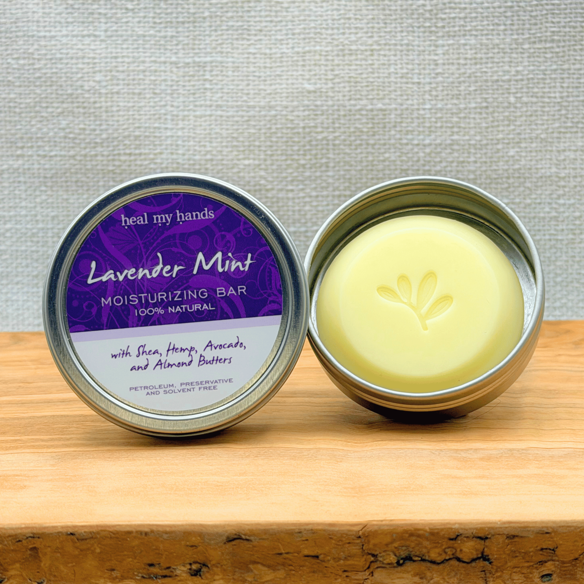 Lavender Mint moisturizing bar in a metal container on a wooden surface with a gray background