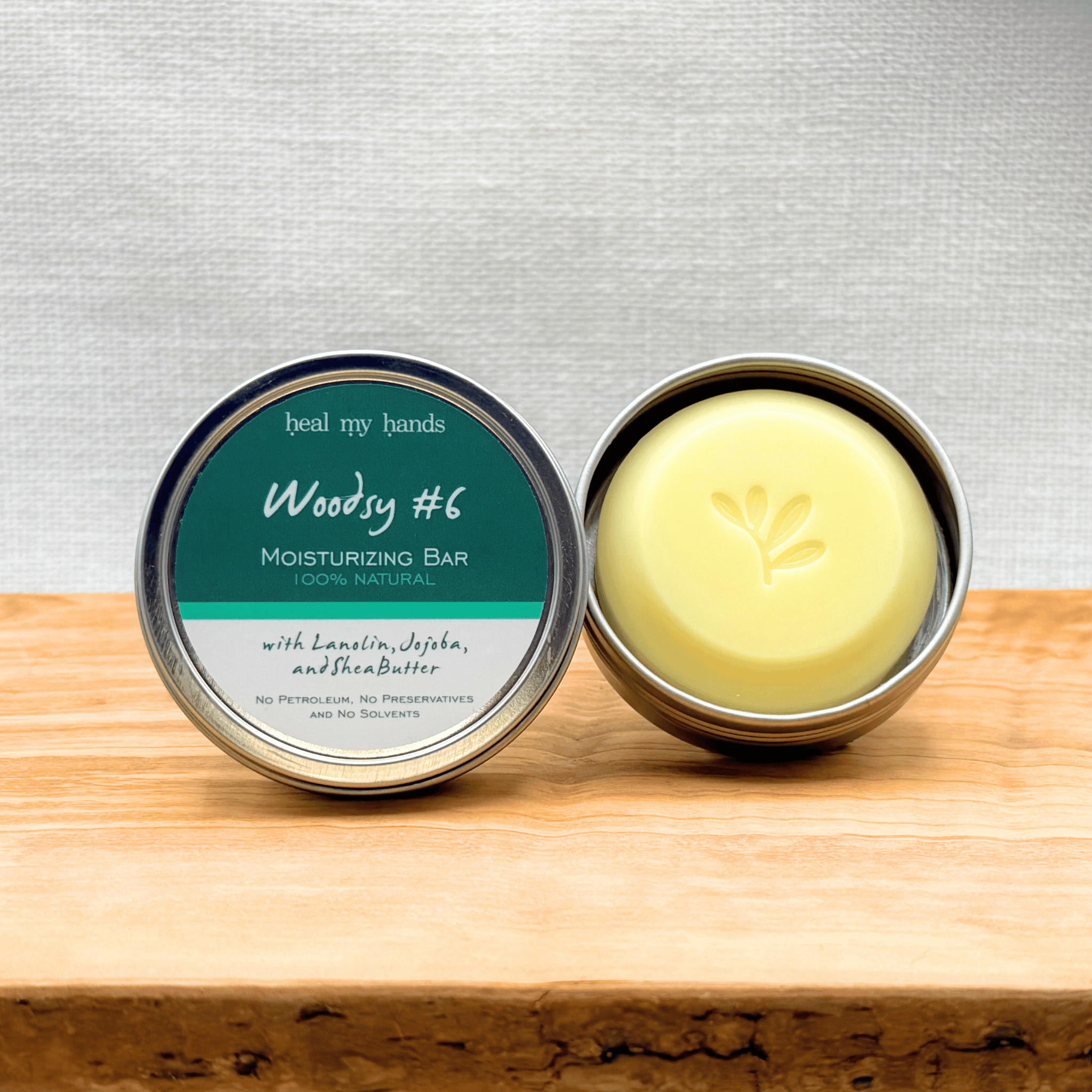 Heal My Hands Moisturizing bar in a tin with 'Woody #6 label on a wooden surface.