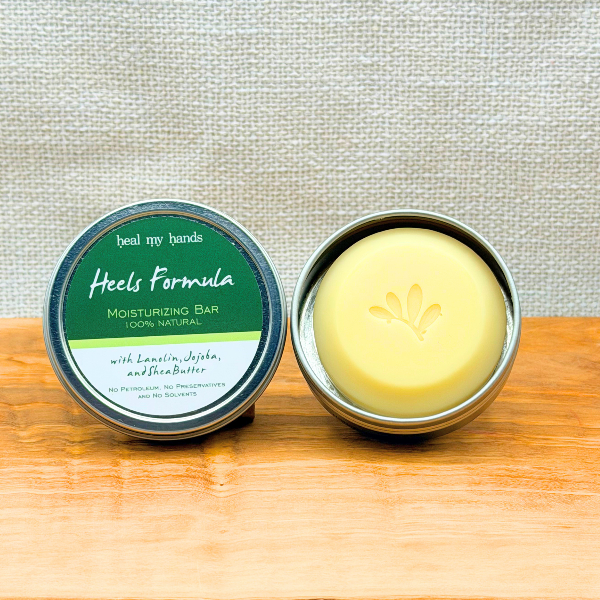 Heal My Hands - Heels Forumla moisturizing bar in a metal container on a wooden surface with a light gray background