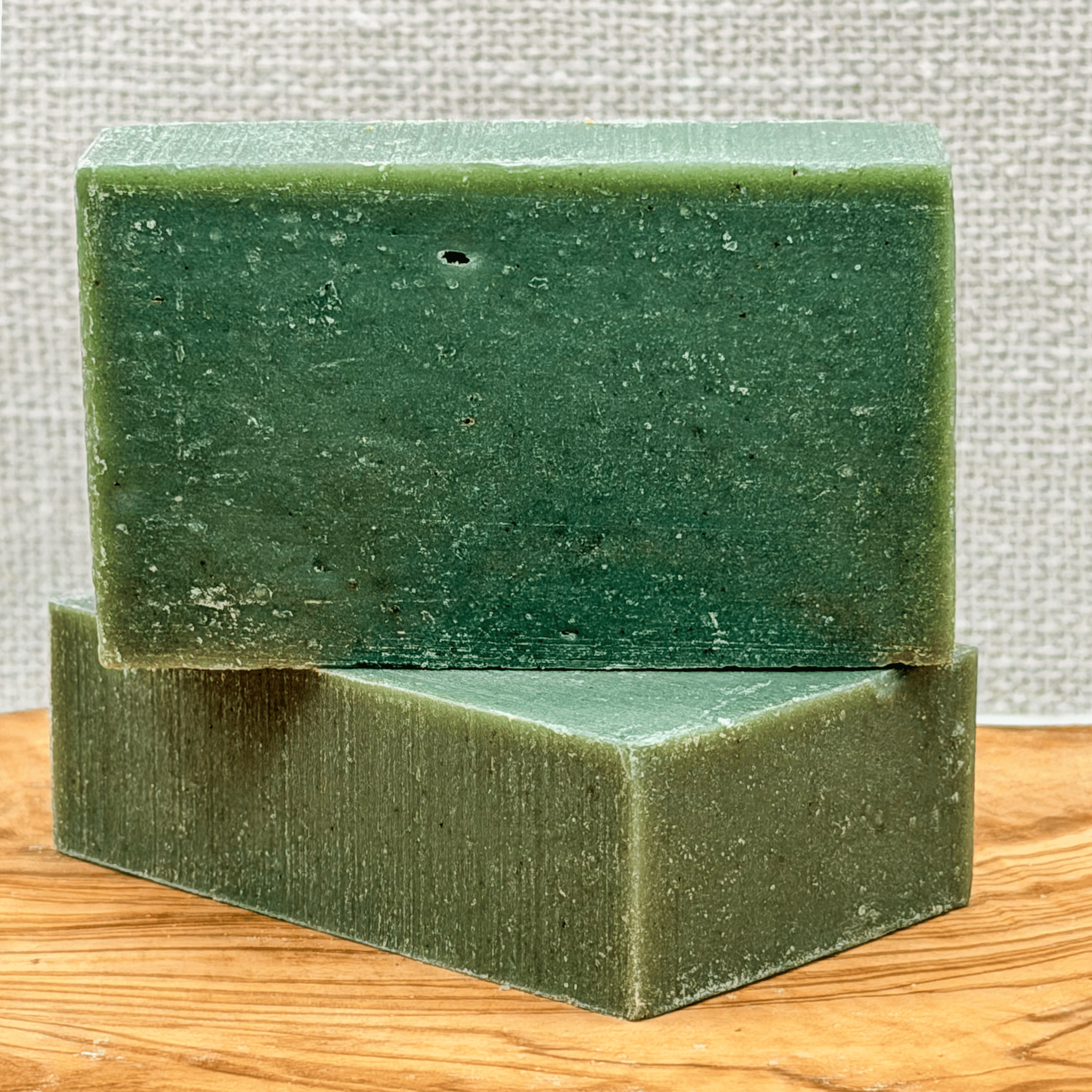 Two green soap bars stacked on a wooden surface with a textured gray background