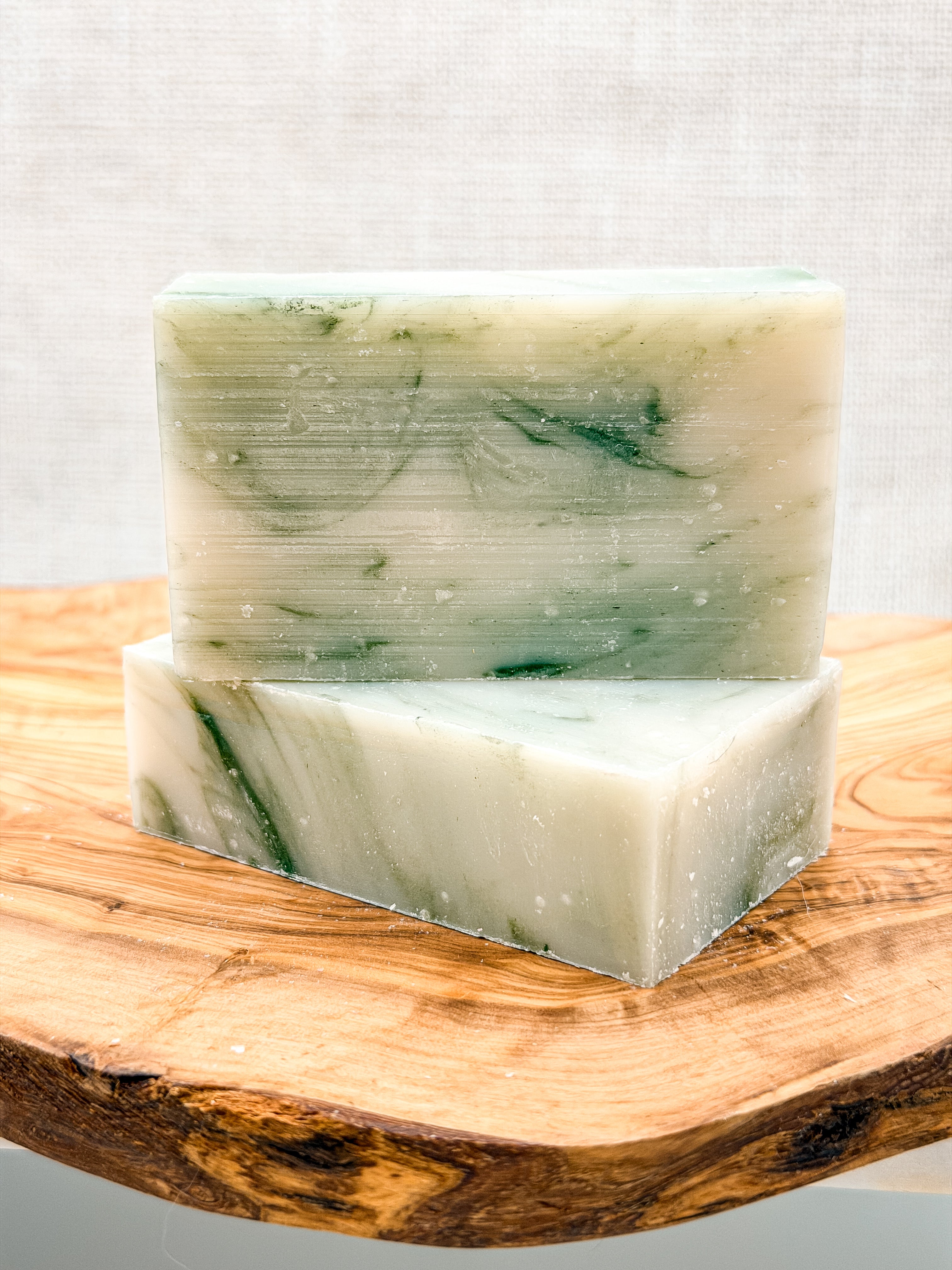 Two bars of green soap on a wooden block with a light gray background