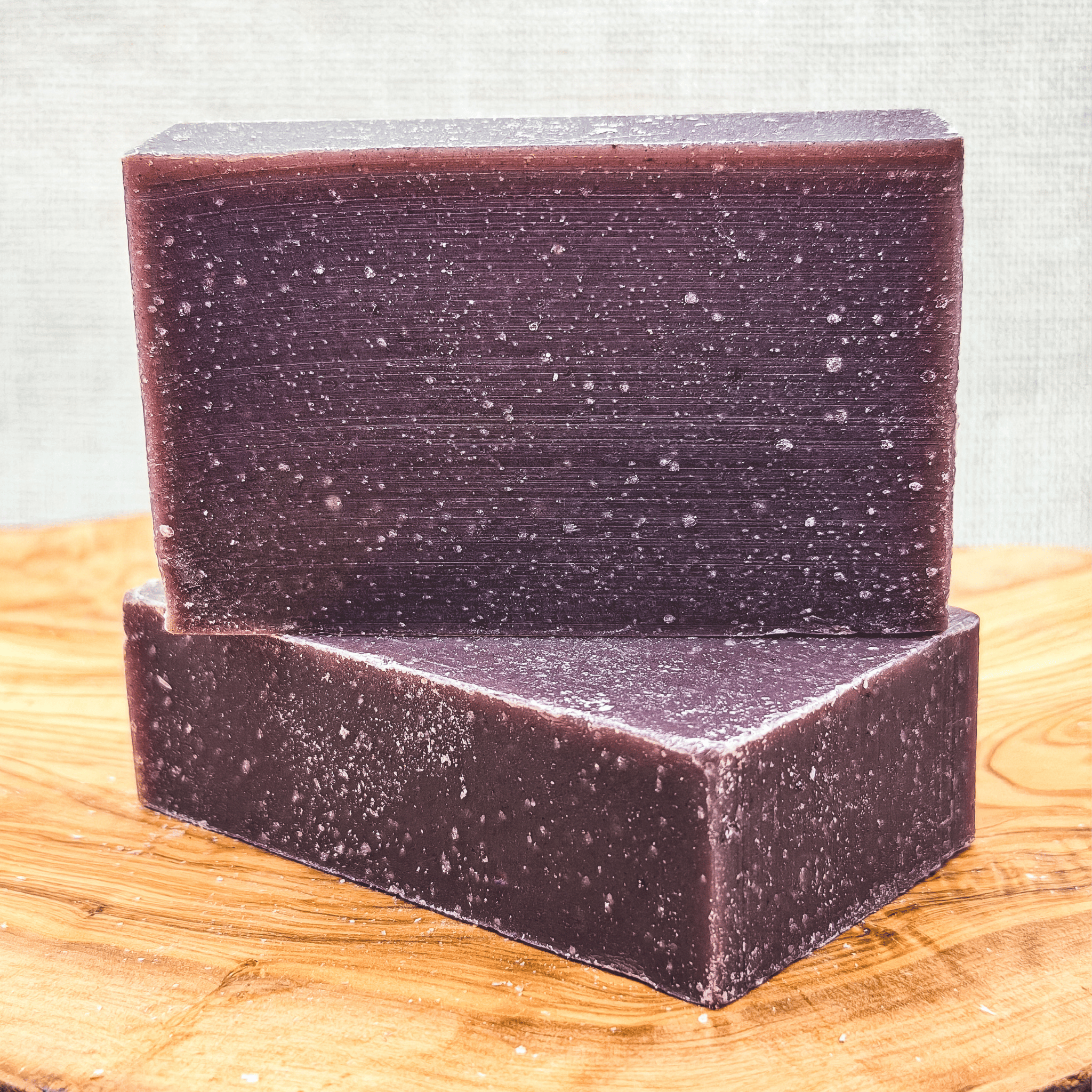 Two purple soap bars stacked on a wooden surface with a textured gray background