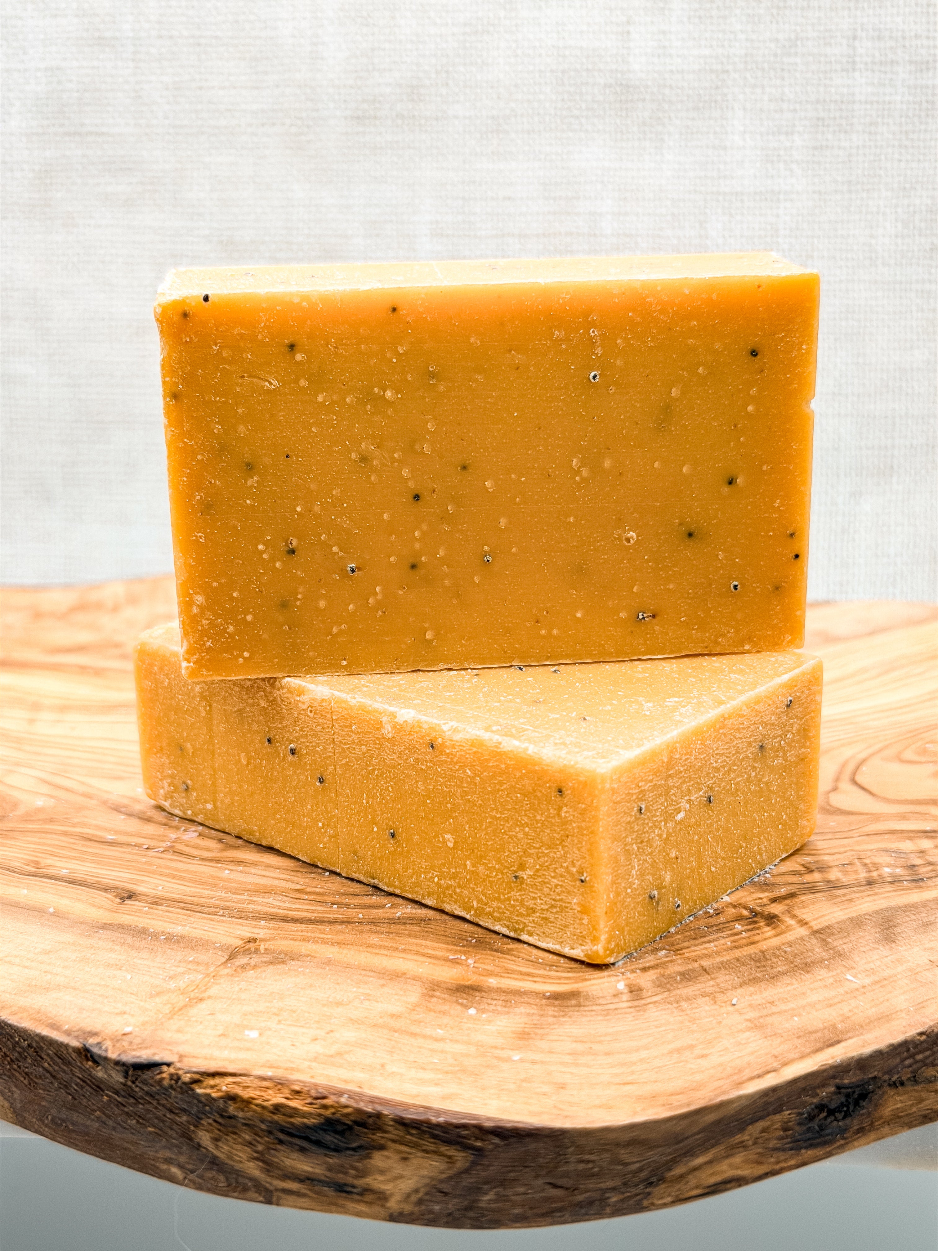 Two bars of yellow soap with specks on a wooden surface against a light gray background