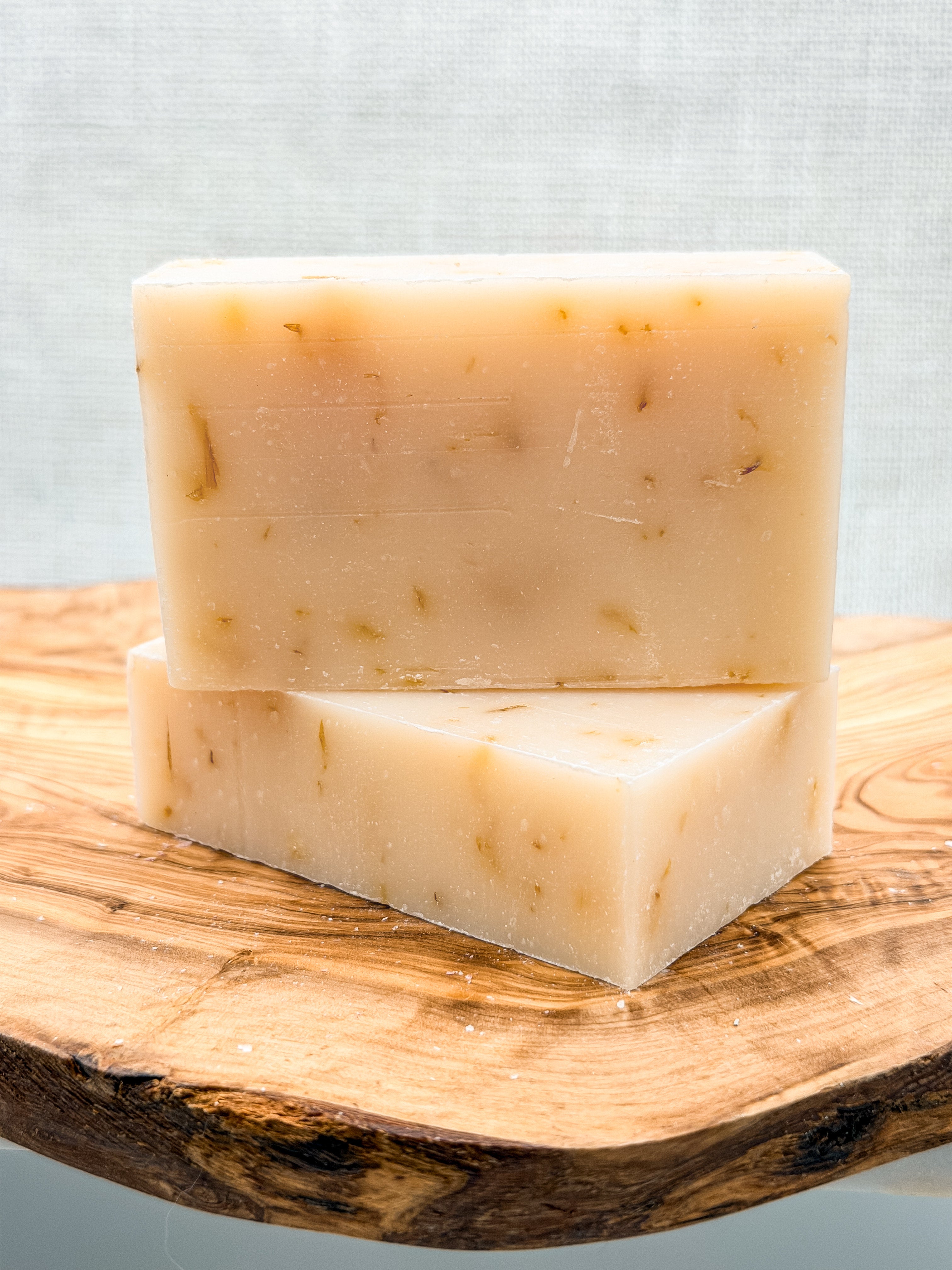 Two bars of soap stacked on a wooden surface with a light gray background