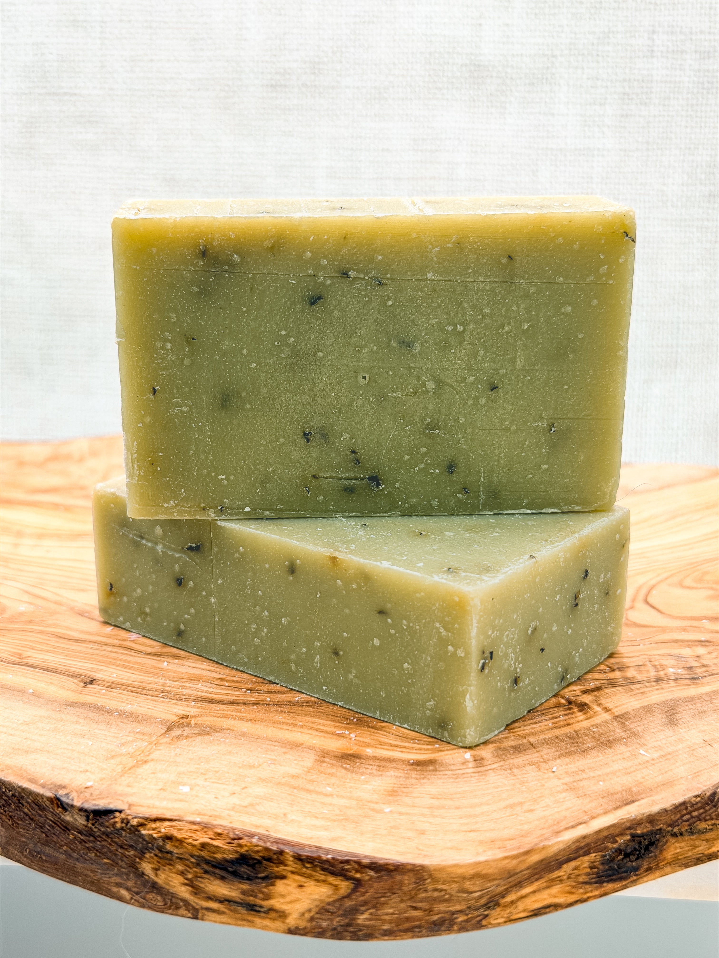 Two green soap bars stacked on a wooden surface with a light gray background