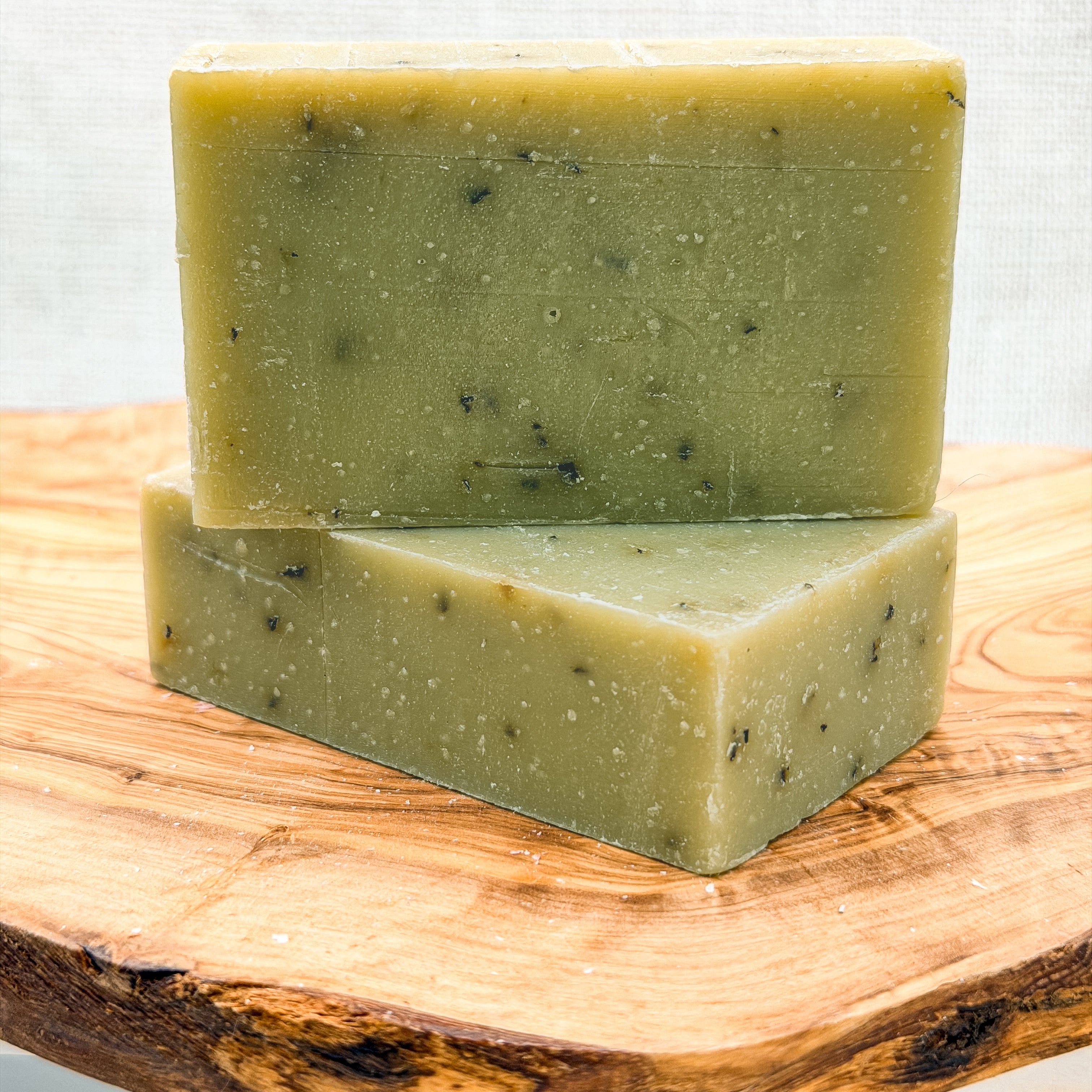 Two green soap bars stacked on a wooden surface with a light gray background