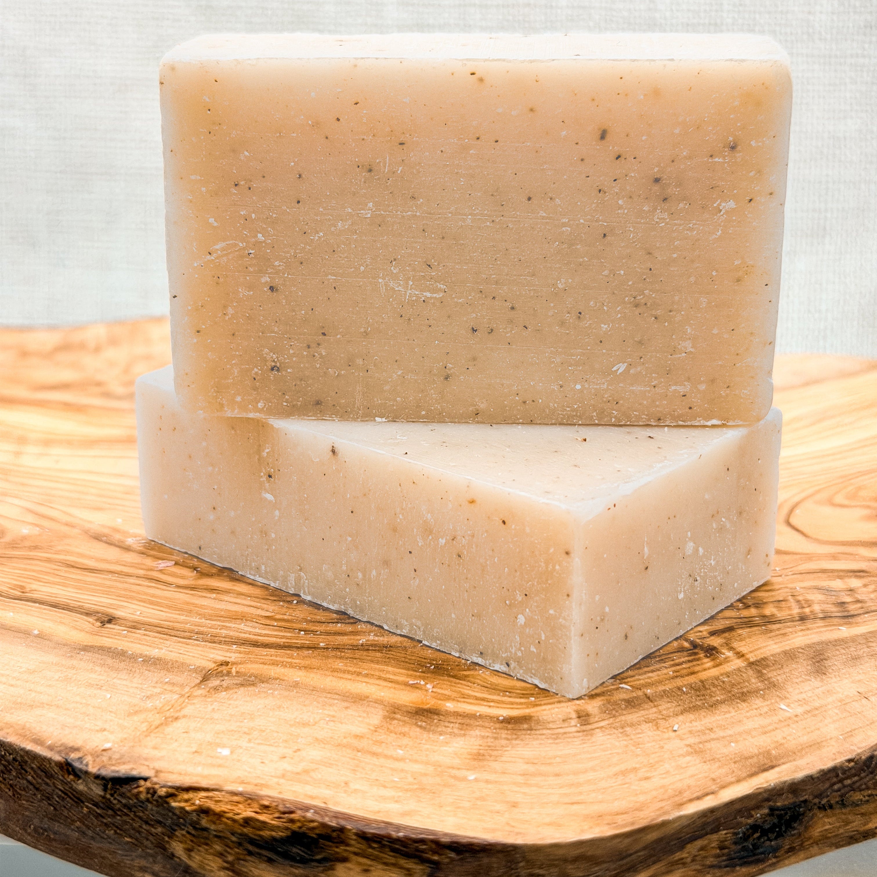 Two bars of soap stacked on a wooden surface with a light gray background