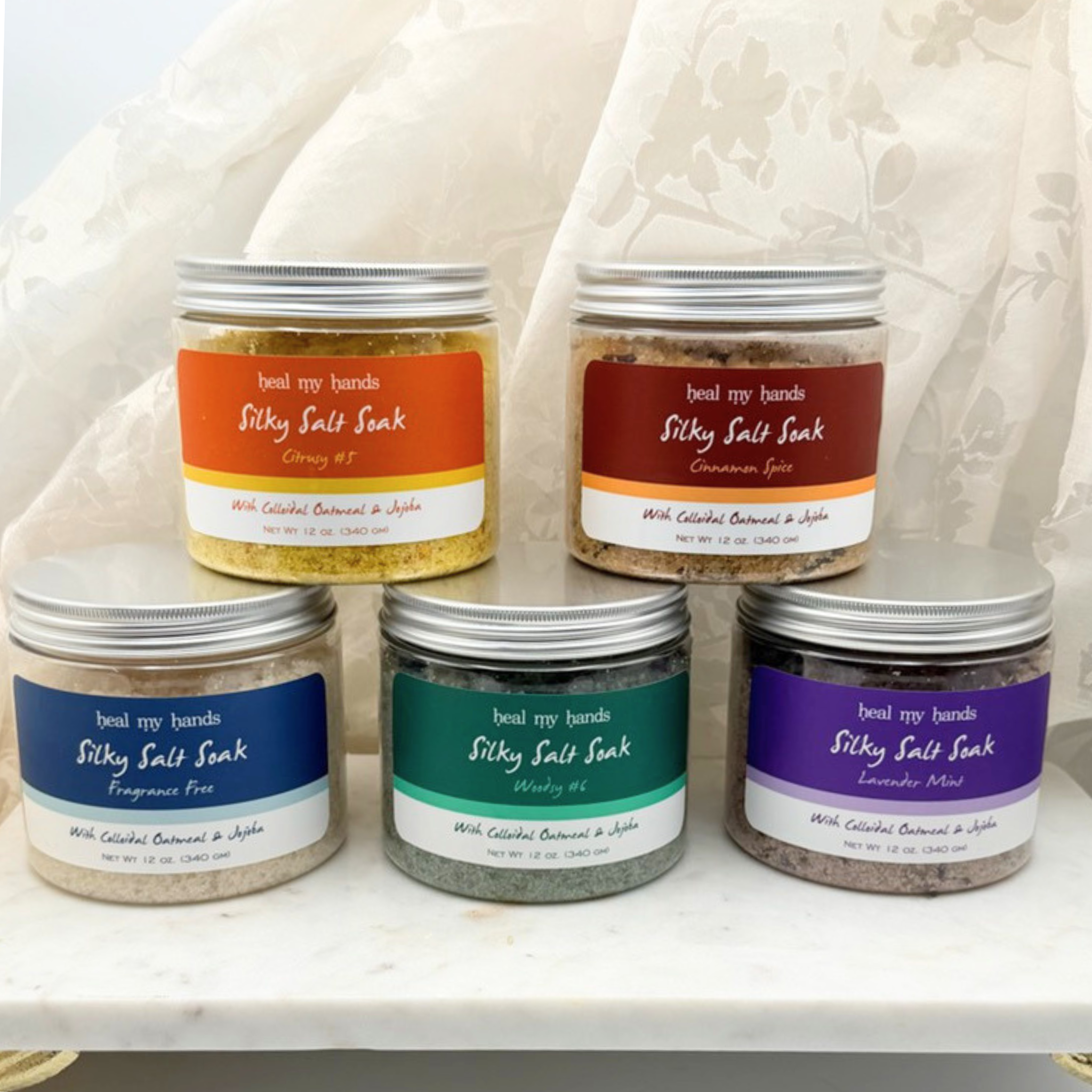 5 jars of Silky Salt Soak in CItrusy #5, Cinnamon Spice, Fragrance Free, Woodsy #6, and Lavender Mint on a marble surface.