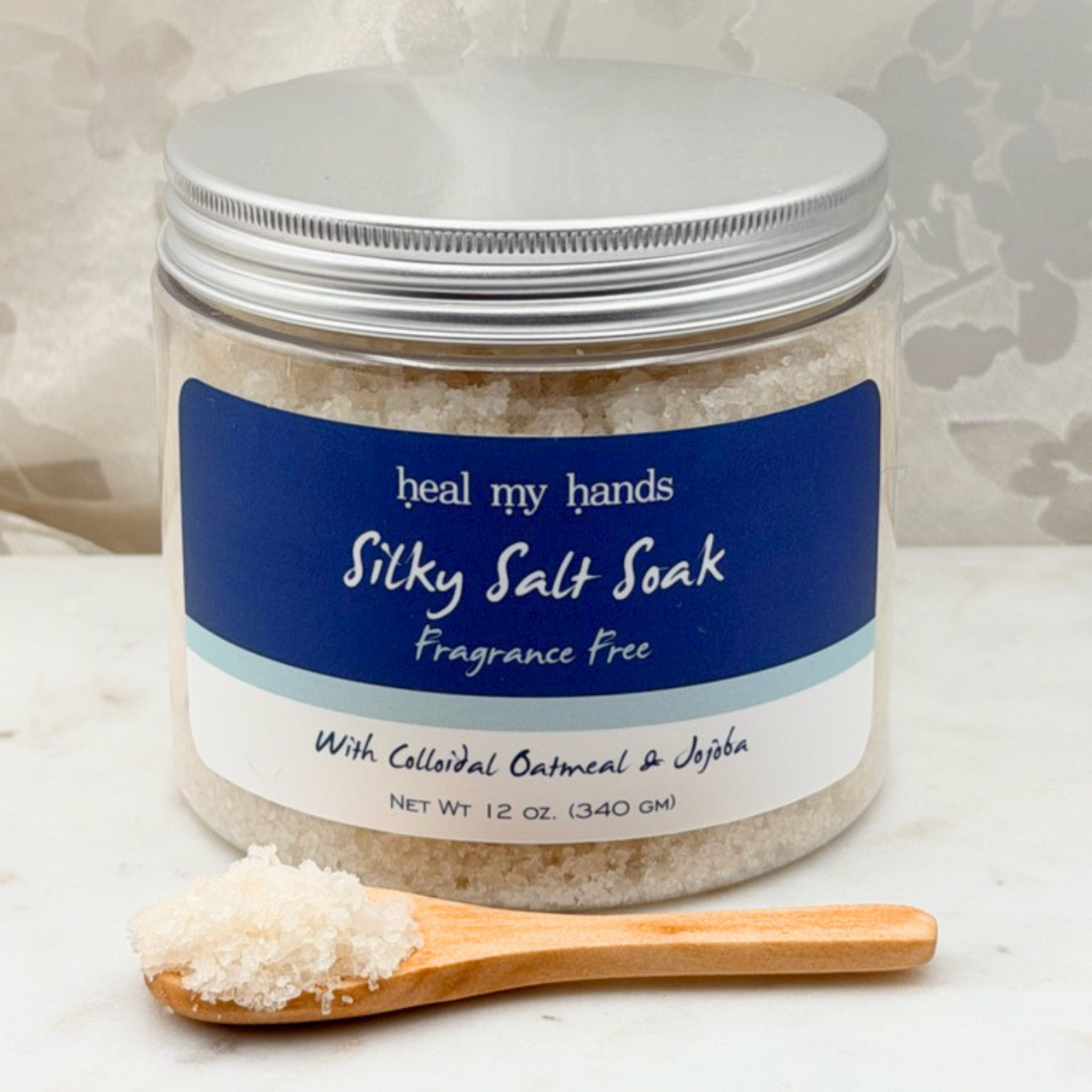 Jar of Fragrance Free Silky Salt Soak with small amount of bath salts on wooden spoon on marble surface.