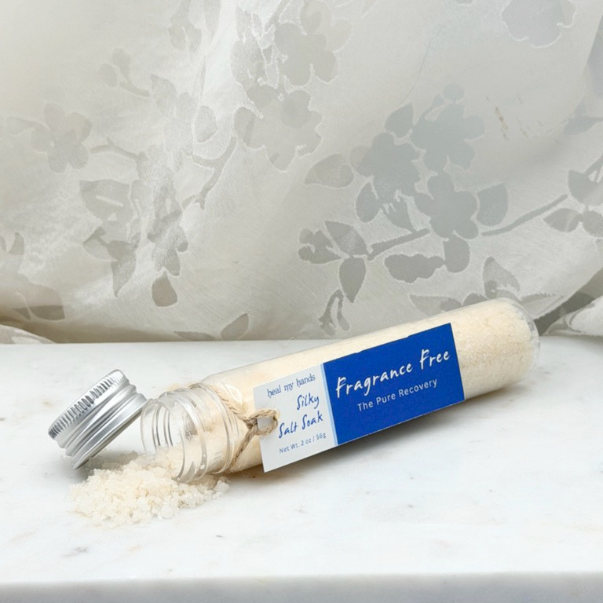 Fragrance Free Silky Salt Soak spilling out of vial on marble surface.