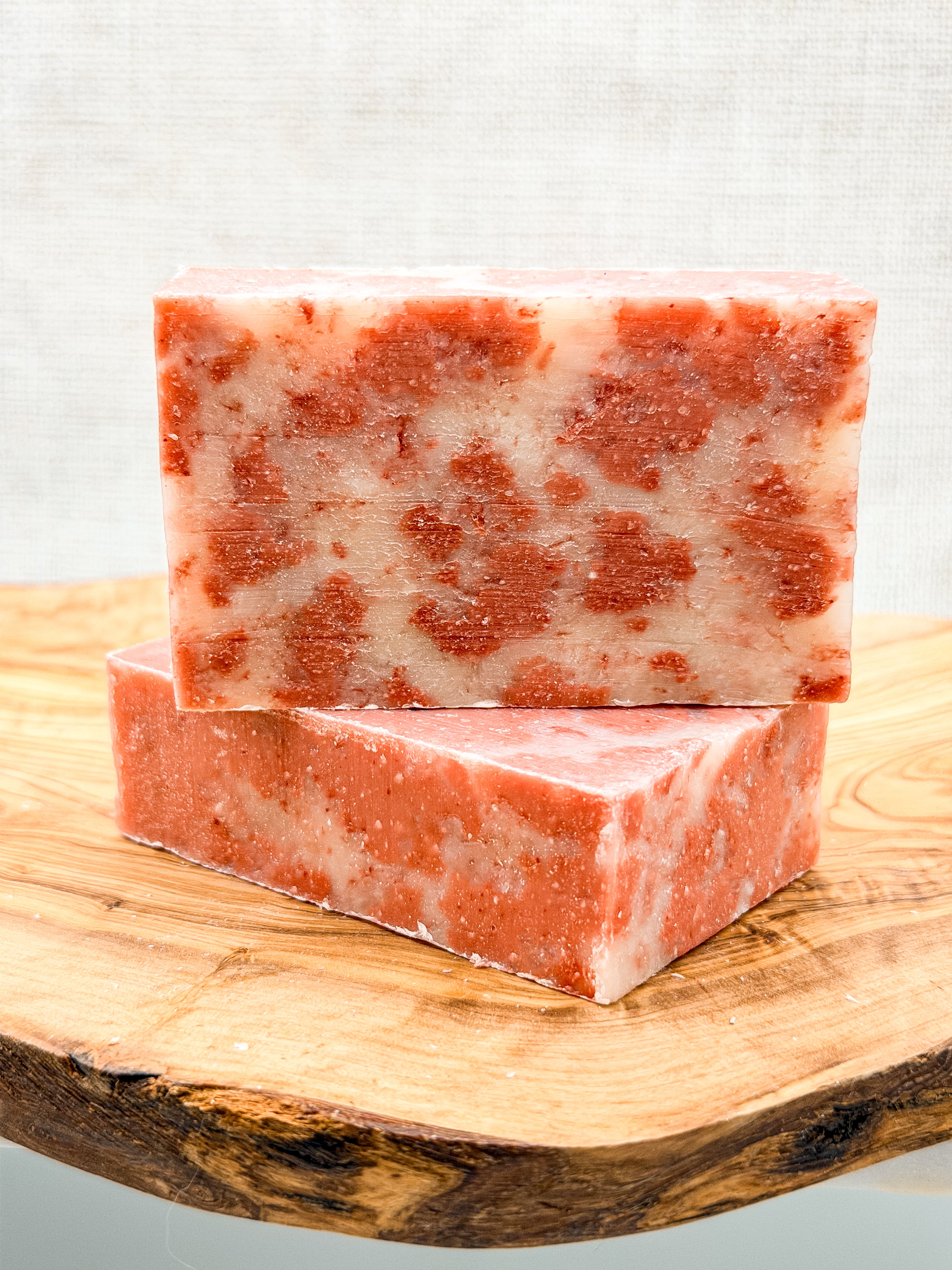 Two pink and white marbled soap bars on a wooden surface with a light gray background