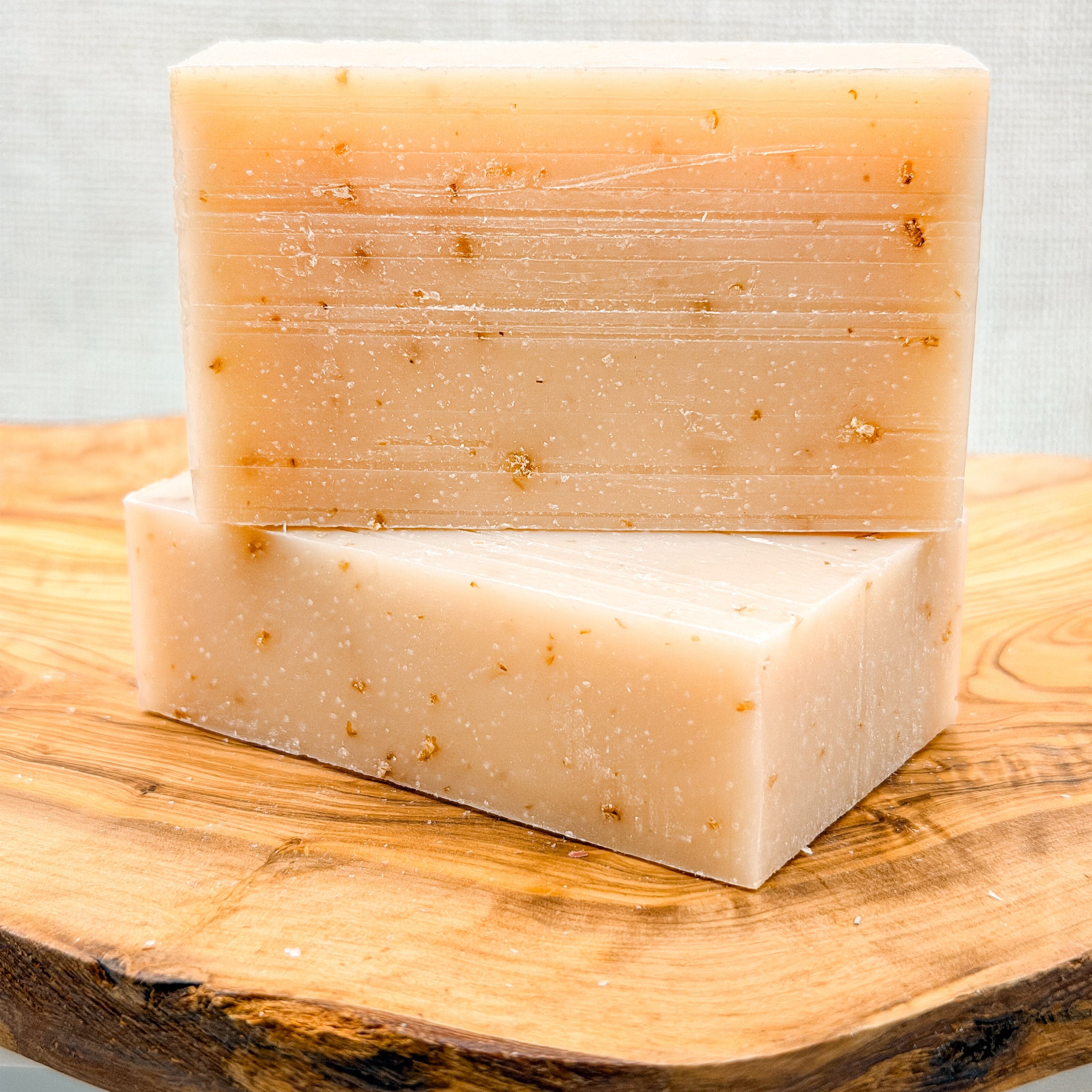 Two bars of soap stacked on a wooden surface with a light gray background