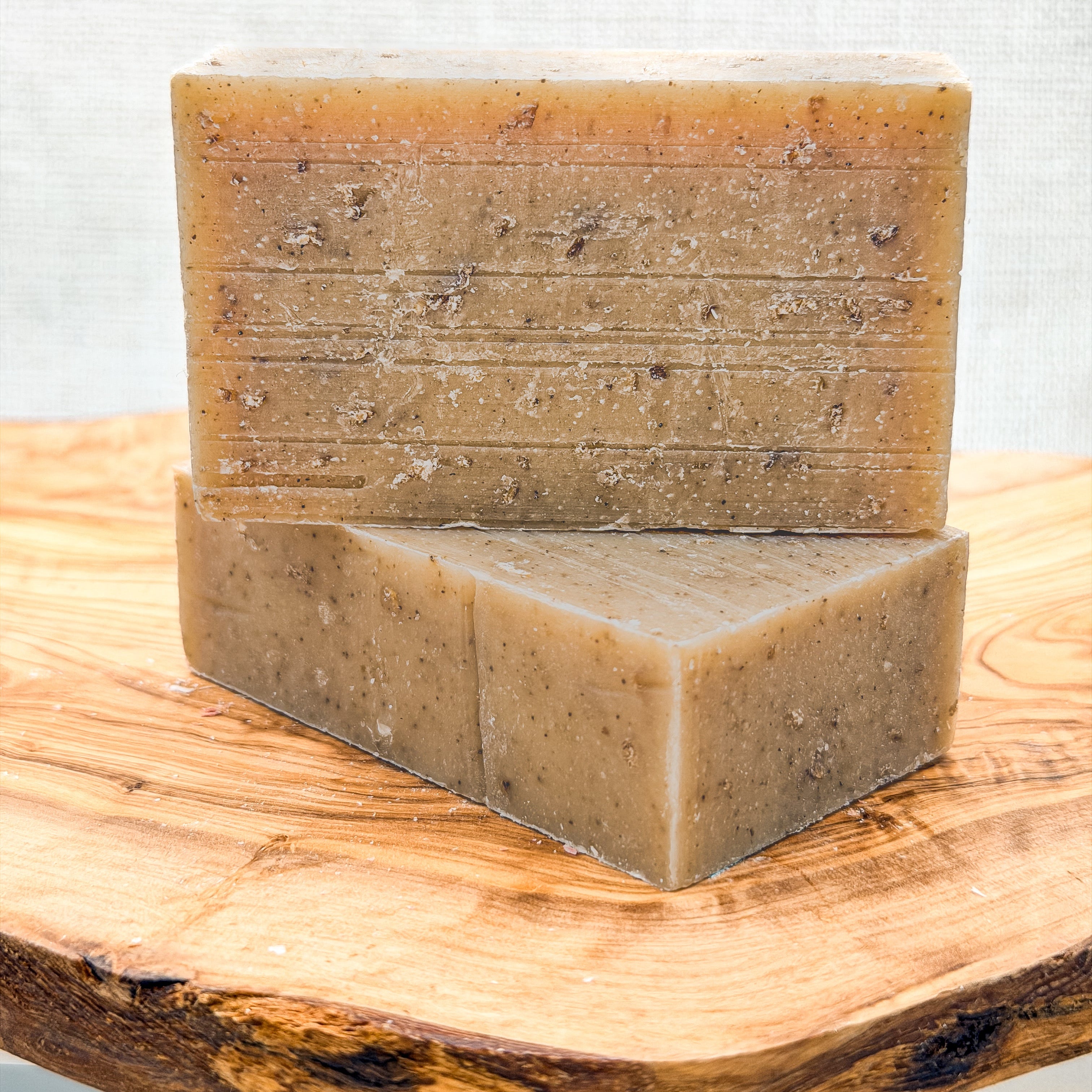 Two bars of brown soap stacked on a wooden surface with a light gray background