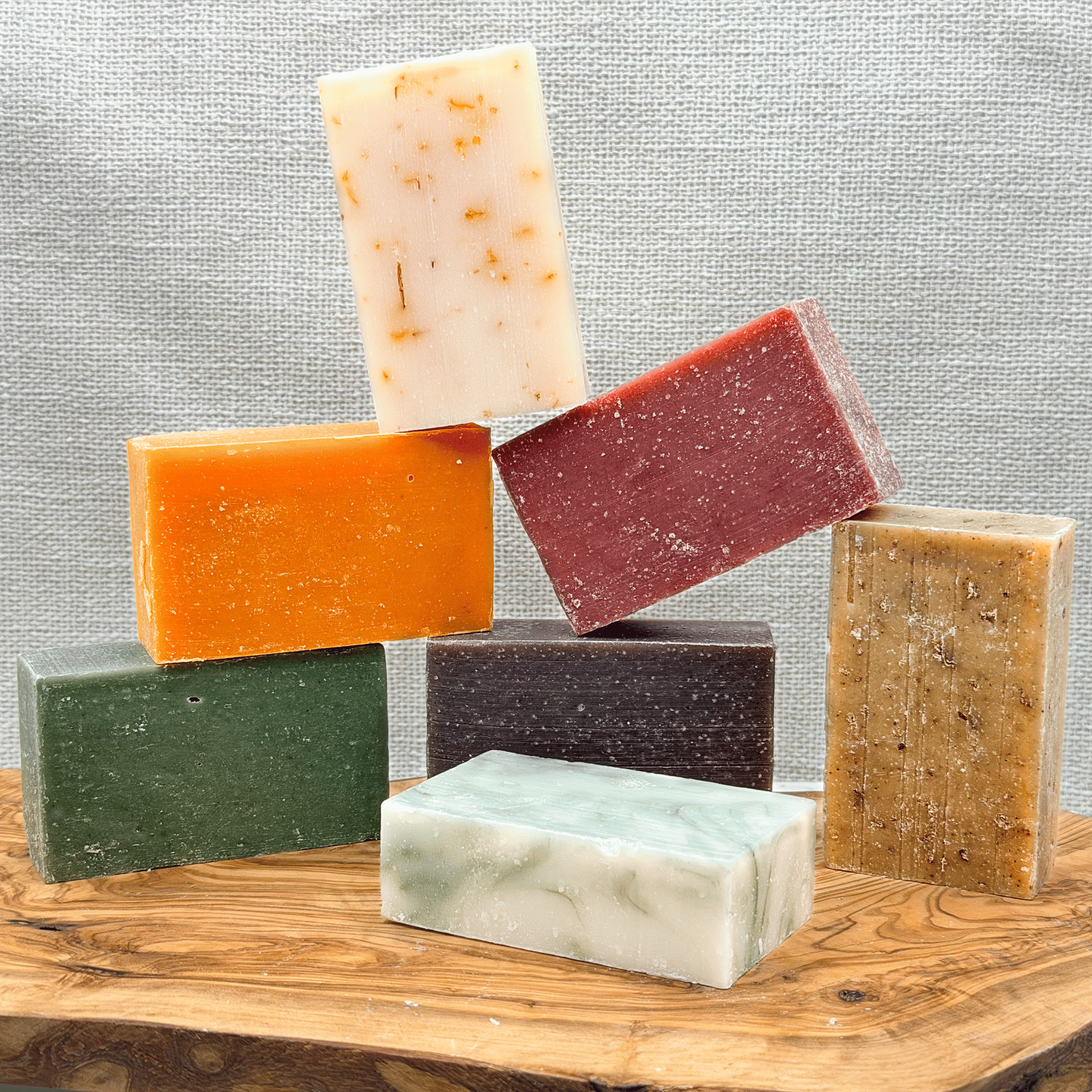 Stack of assorted soaps on a wood surface with a linen background.