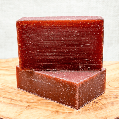 Two brown soap bars stacked on a wooden surface with a light gray background