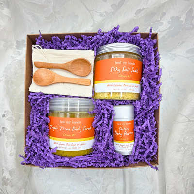 Box filled with purple crinkle paper and a jar of Silky Salt Soak, Triple Treat Body Scrub, and Better Body Butter in Citrusy #5 with two small wooden spoons and a muslin pouch.