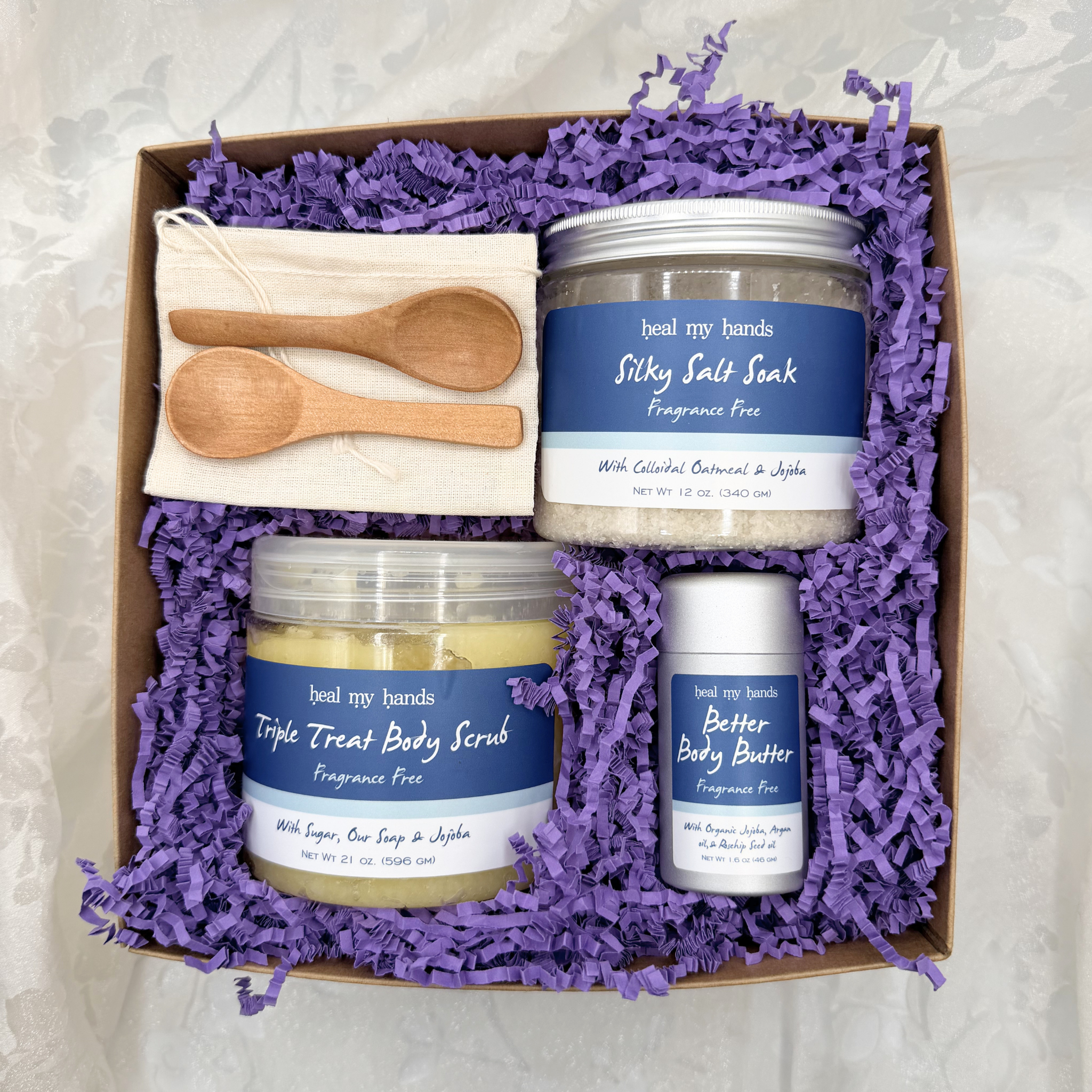 Box filled with purple crinkle paper and a jar of Silky Salt Soak, Triple Treat Body Scrub, and Better Body Butter in Fragrance Free with two small wooden spoons and a muslin pouch.
