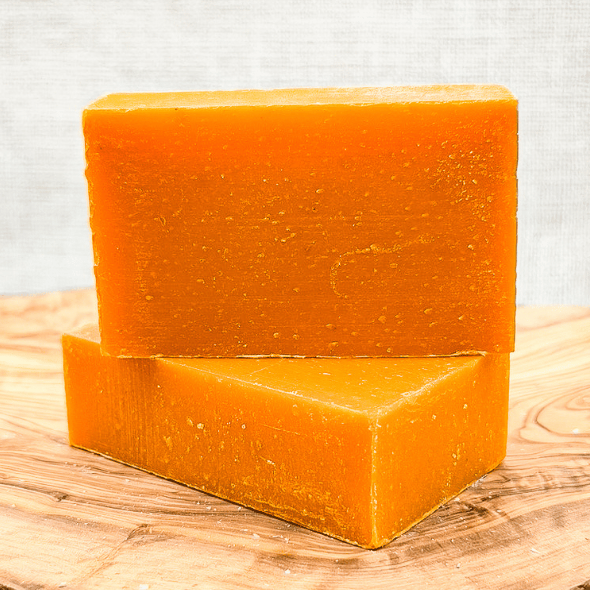 Two orange soap bars on a wooden surface with a light gray background