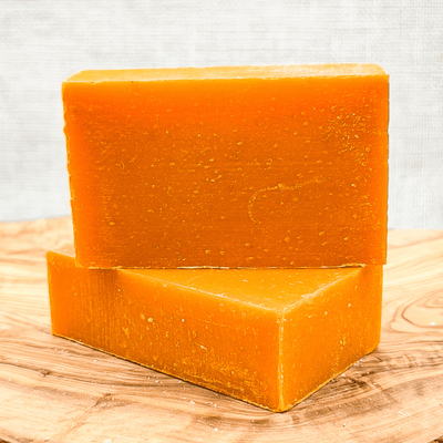 Two orange soap bars on a wooden surface with a light gray background