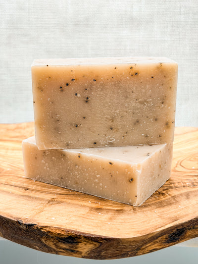 Two bars of soap stacked on a wooden surface with a light background