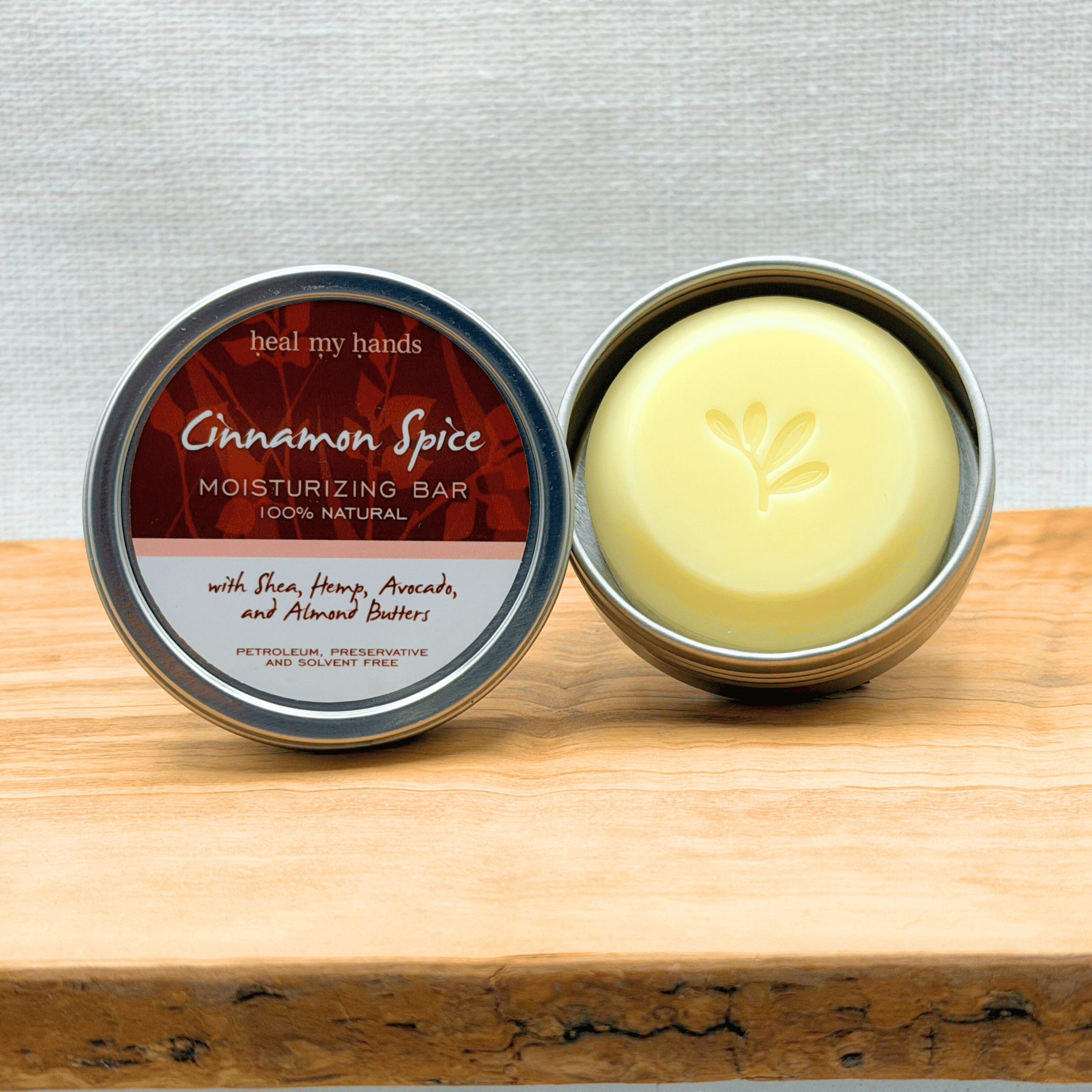 Cinnamon Spice moisturizing bar in a metal container on a wooden surface with a gray background