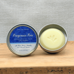 Fragrance-free moisturizing bar in a metal container on a wooden surface with a gray textured background.