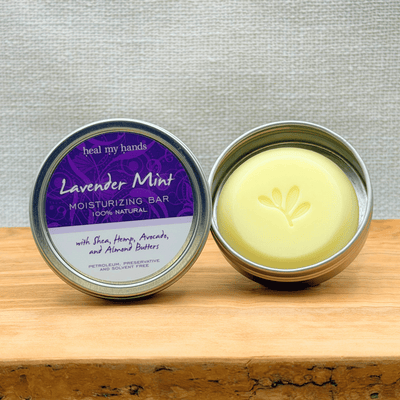 Lavender Mint moisturizing bar in a metal container on a wooden surface with a gray background