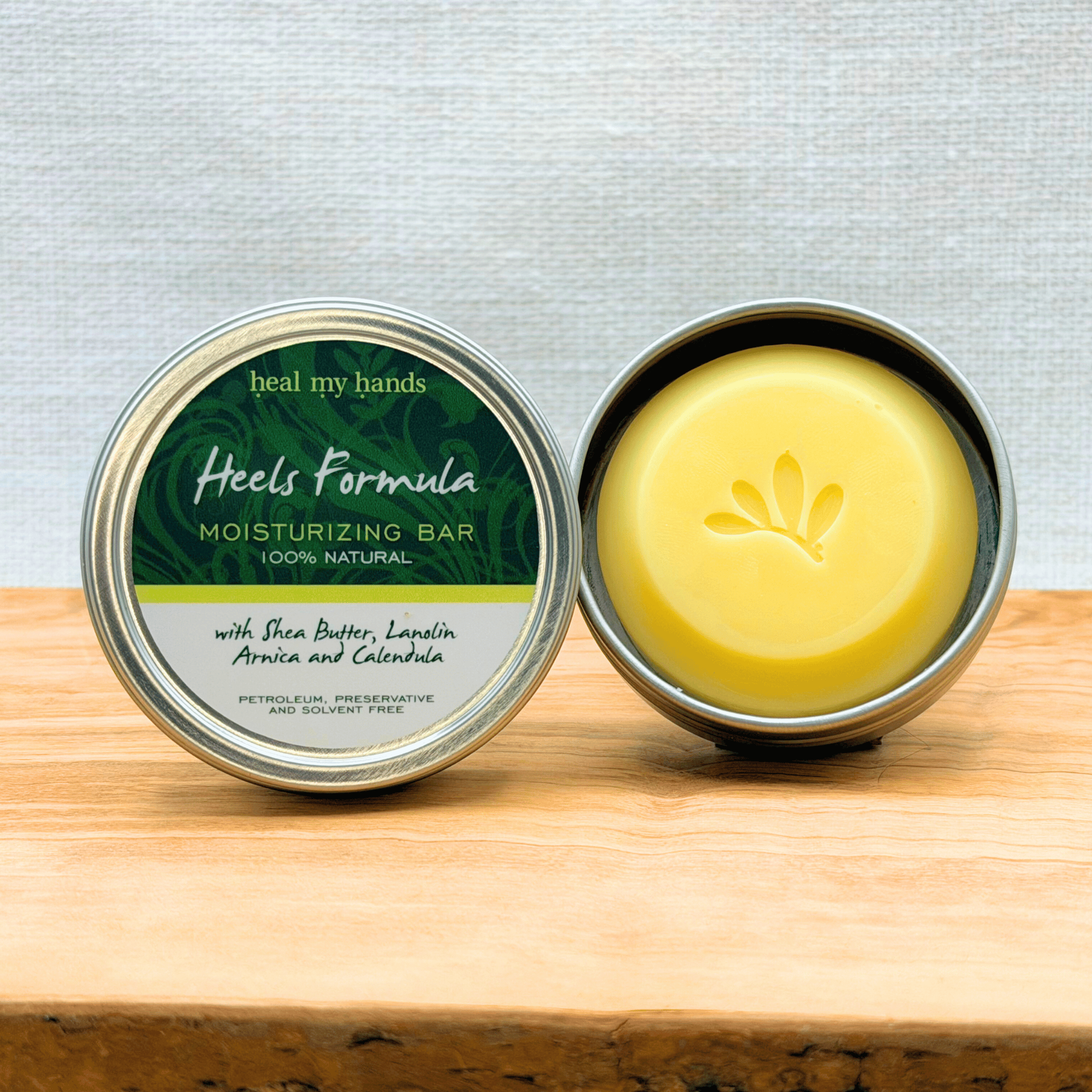 Heal My Hands - Heels Forumla moisturizing bar in a metal container on a wooden surface with a light gray background