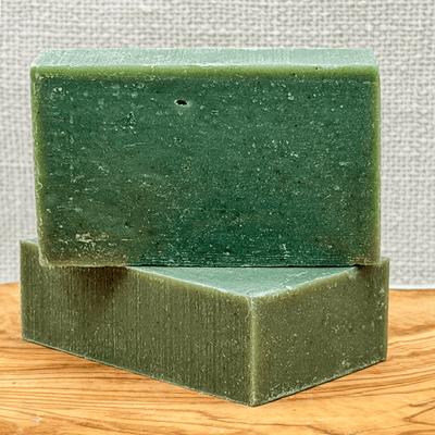 Two green soap bars stacked on a wooden surface with a textured gray background