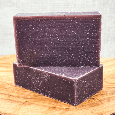 Two purple soap bars stacked on a wooden surface with a textured gray background