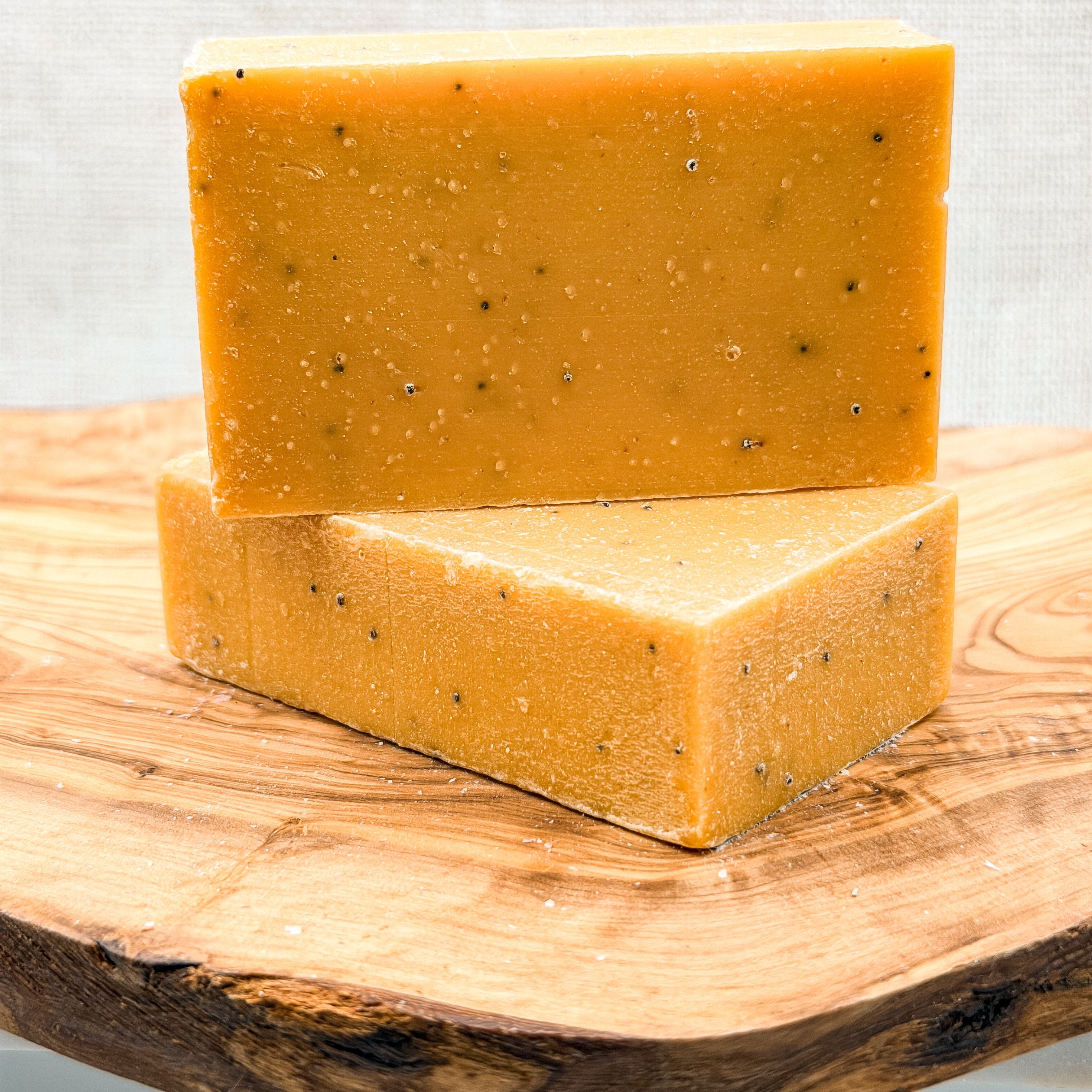 Two bars of yellow soap with specks on a wooden surface against a light gray background