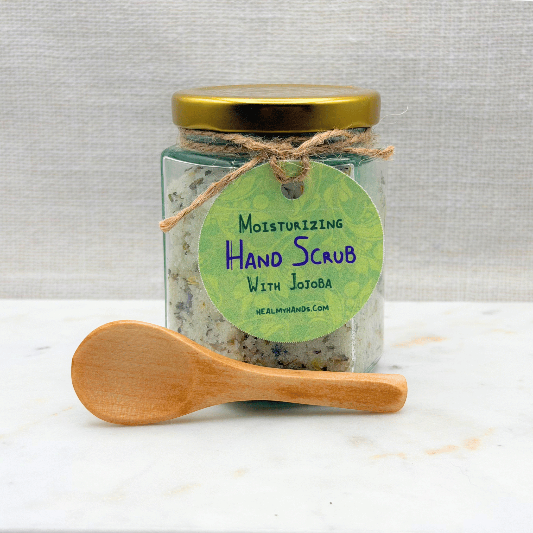 Jar of moisturizing hand scrub with a wooden spoon on a white surface
