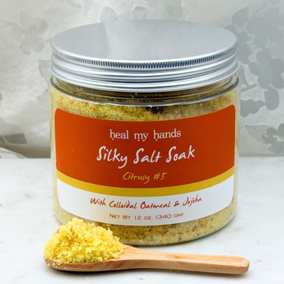 Jar of Citrusy #6 Silky Salt Soak with small amount of bath salts on wooden spoon on marble surface.