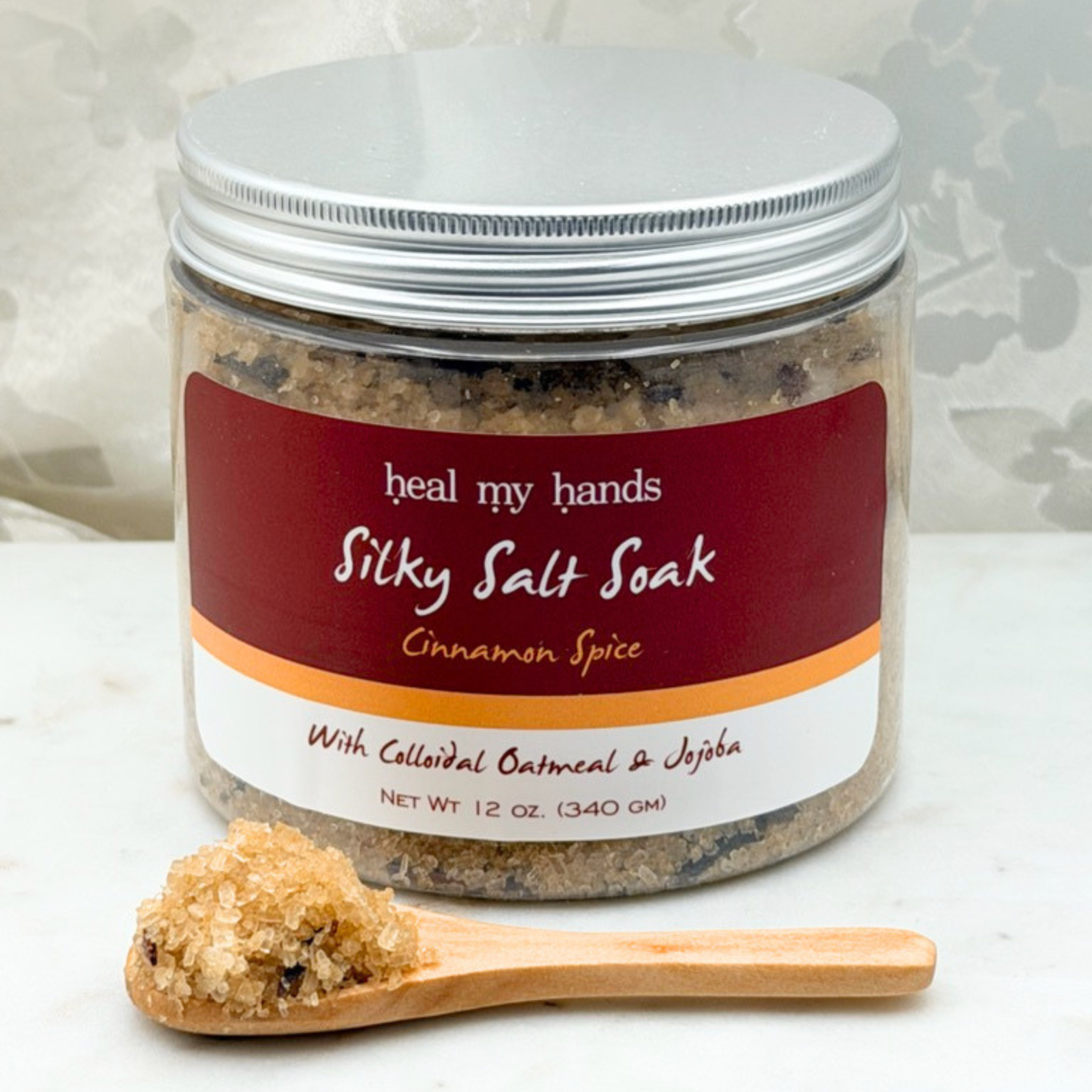 Jar of Cinnamon Spice Silky Salt Soak with small amount of bath salts on wooden spoon on marble surface.