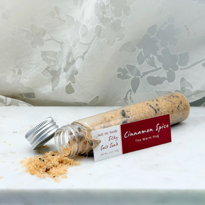 Cinnamon Spice Silky Salt Soak spilling out of vial on marble surface.