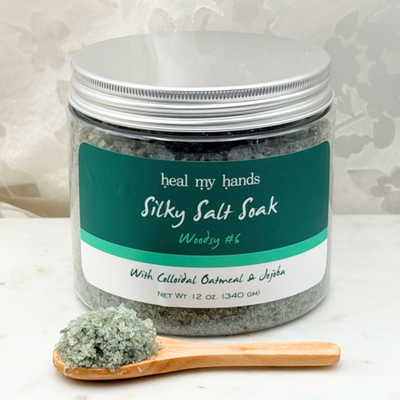 Jar of Woodsy #6 Silky Salt Soak with small amount of bath salts on wooden spoon on marble surface.