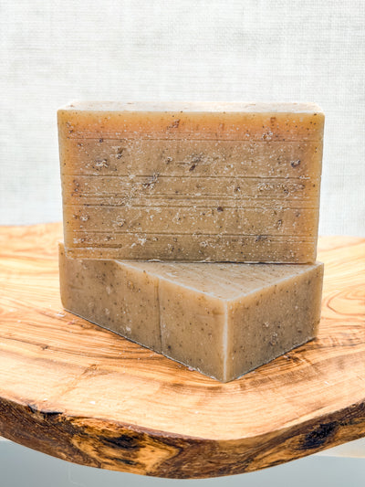 Two bars of brown soap stacked on a wooden surface with a light gray background