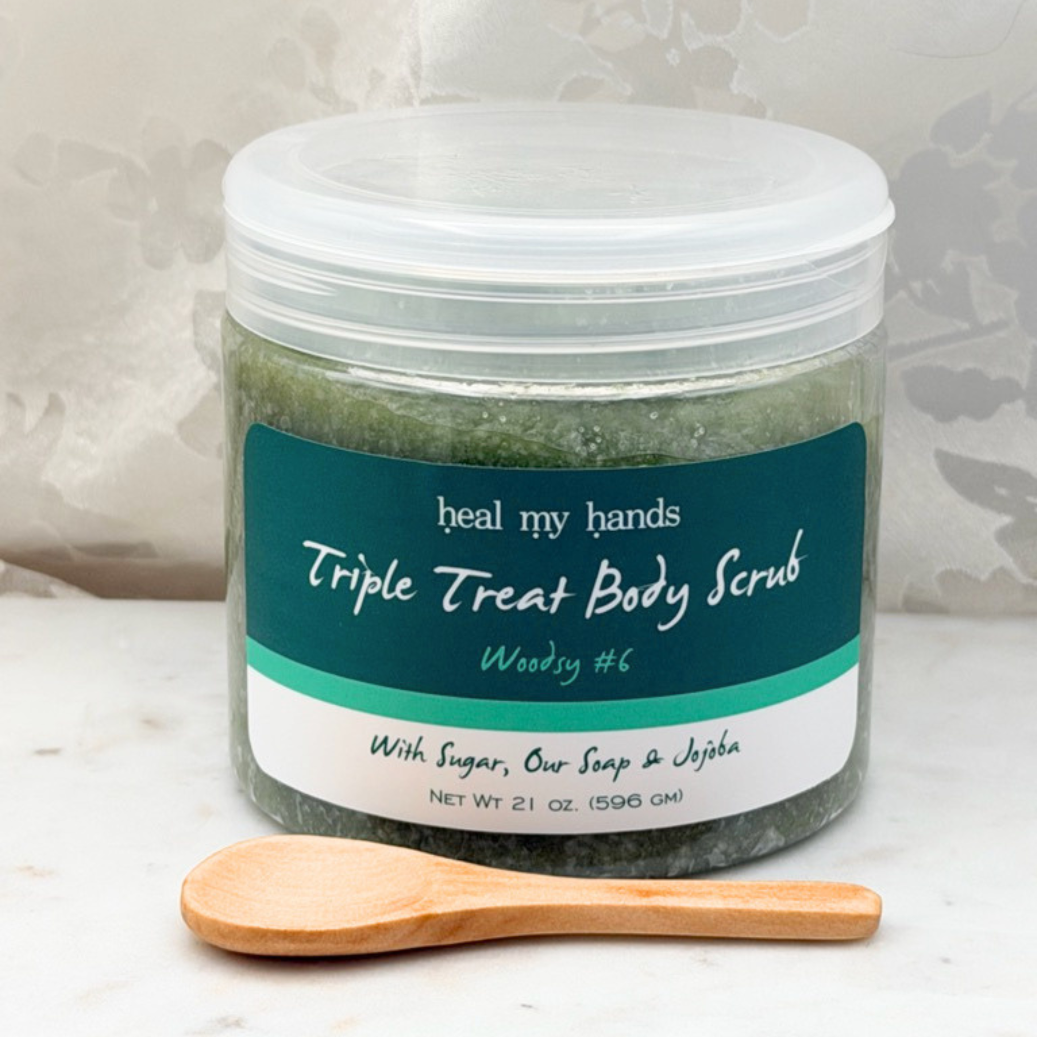 Woodsy #6 Triple Treat Body Scrub jar and small wooden spoon on marble surface.