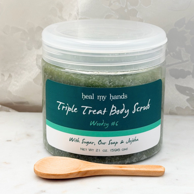 Woodsy #6 Triple Treat Body Scrub jar and small wooden spoon on marble surface.