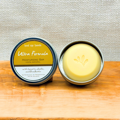 Heal My Hands Ultra Strength Moisturizing bar in a metal container on a wooden surface with a light gray background