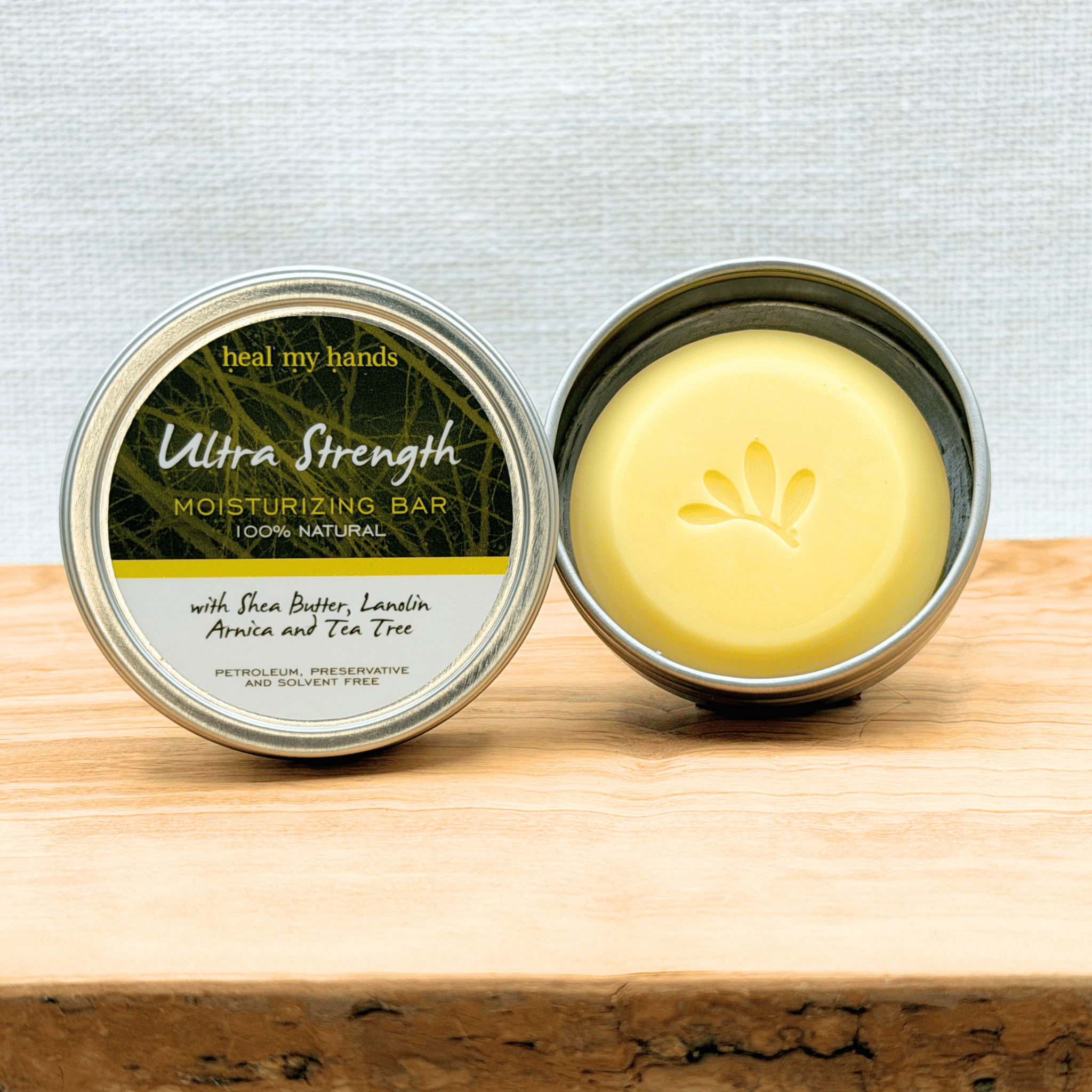 Heal My Hands Ultra Strength Moisturizing bar in a metal container on a wooden surface with a light gray background